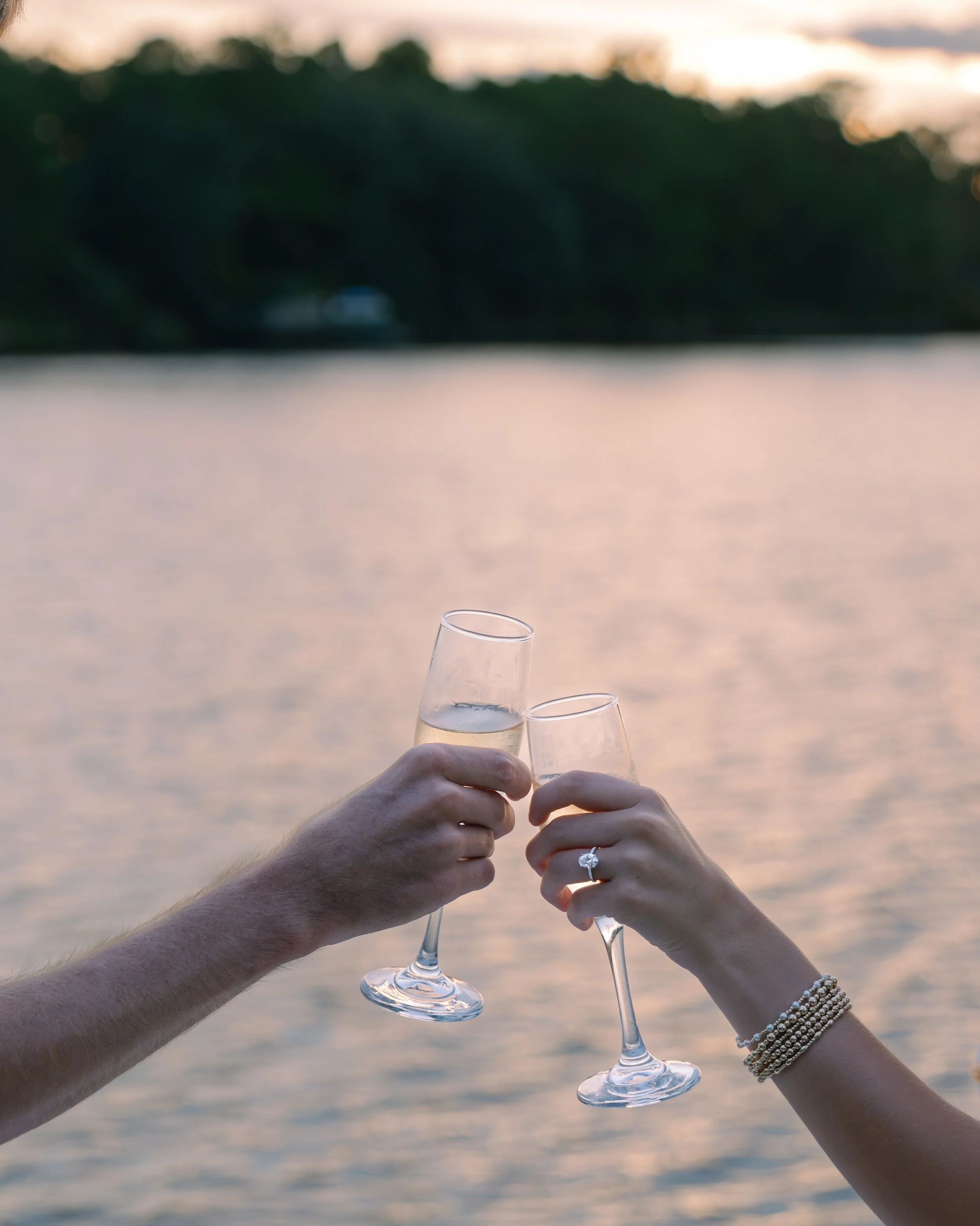 Man and woman cheers with glasses of champagne in the sunset, showing engagement ring. 30A Photographer