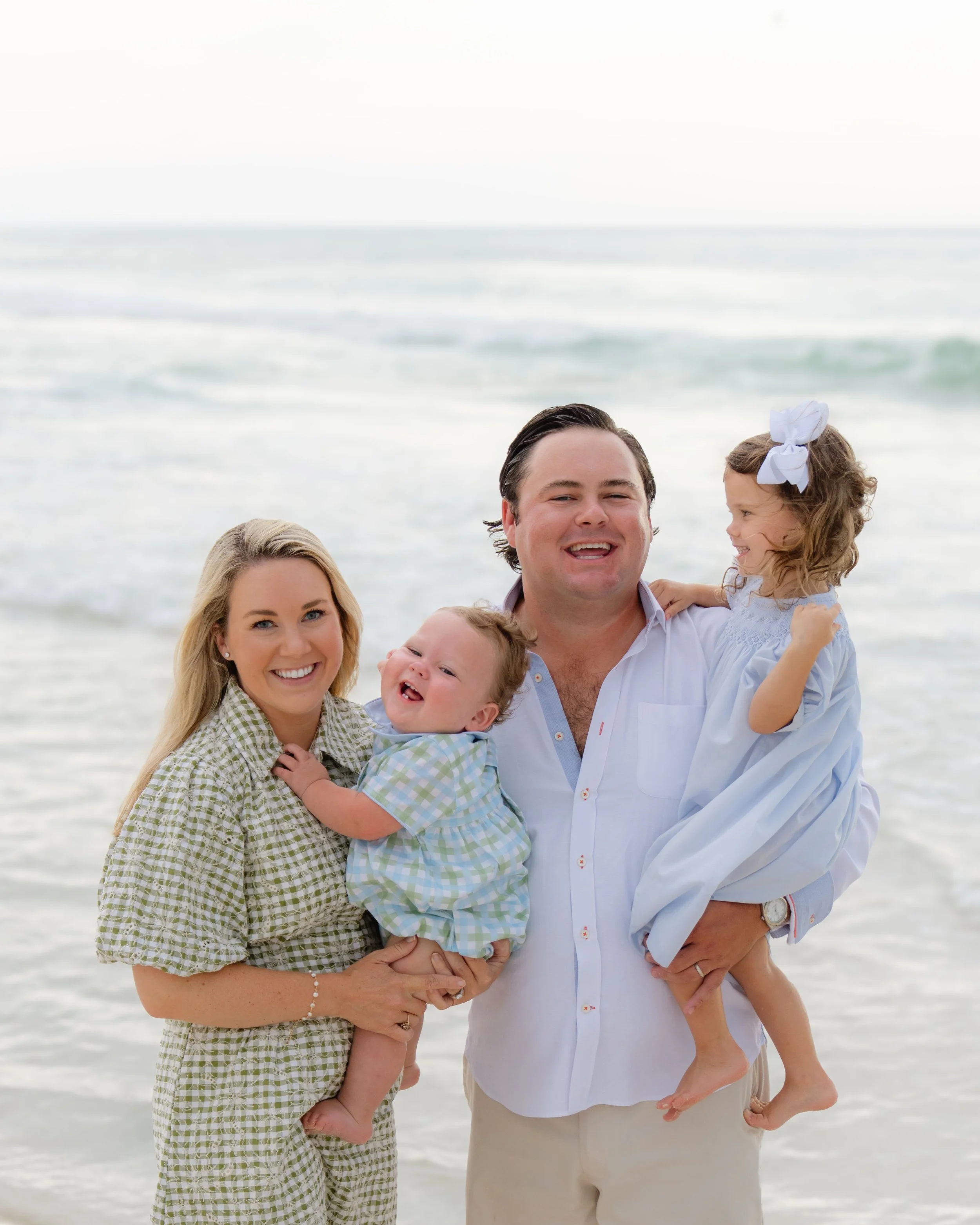 A family of four enjoying time at the beach, smiling and playing near the ocean.