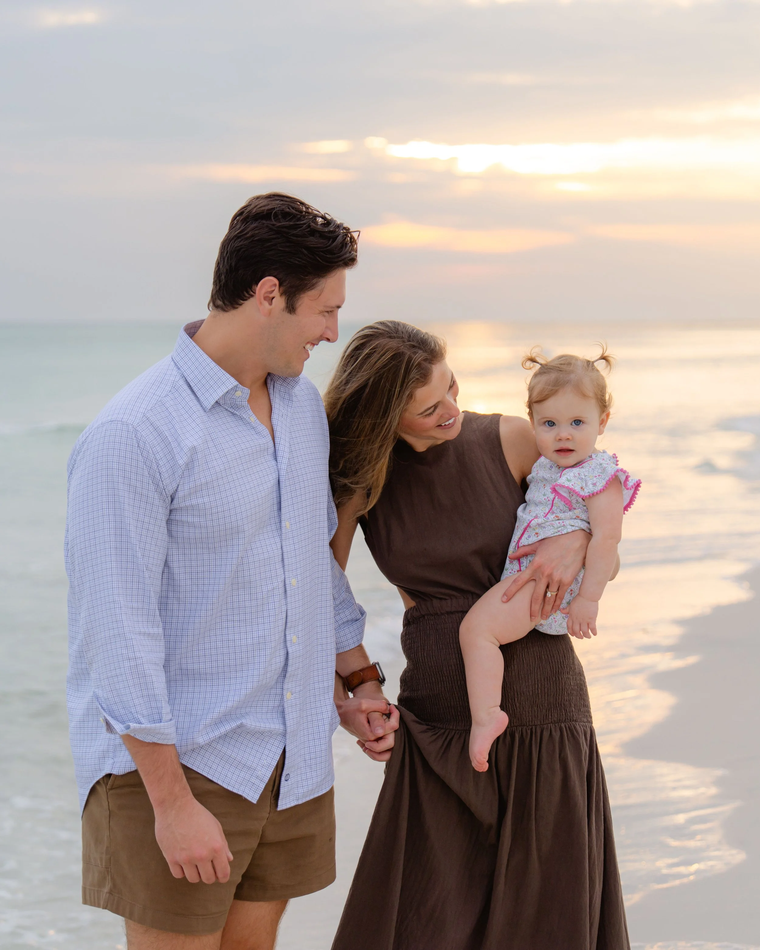 A family of three enjoying a walk on the beach at sunset, with a man and woman holding a young girl.