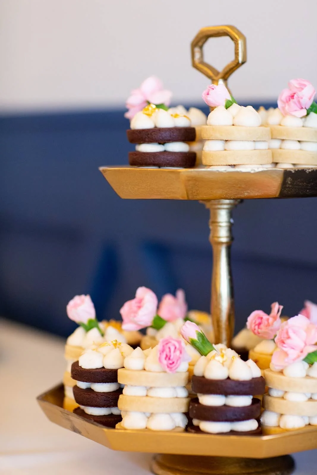 A two-tiered gold dessert stand with cookies decorated with pink flowers and white frosting.
