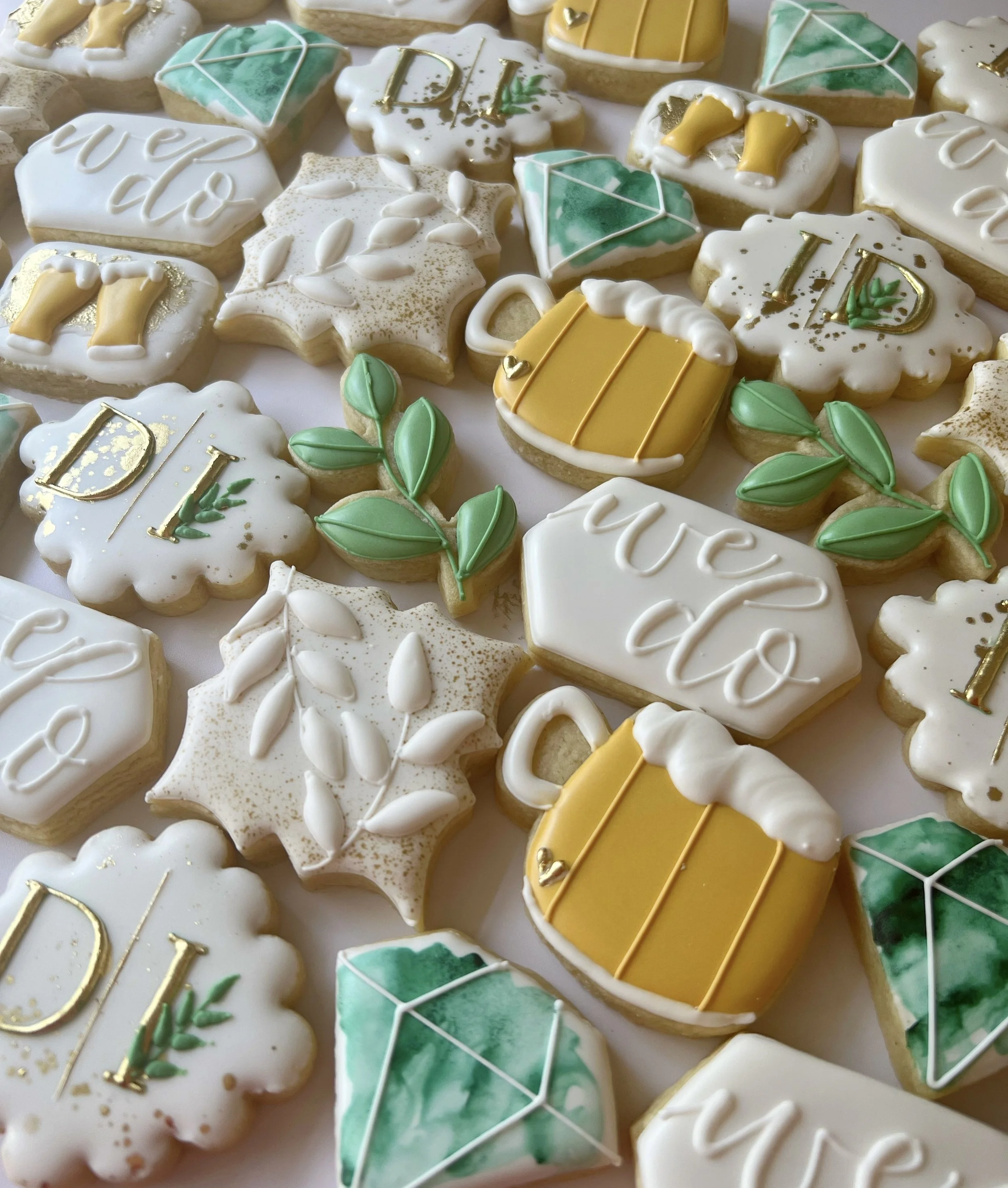 A collection of decorated cookies with Easter and spring themes, including eggs, bunnies, leaves, and the phrase 'Happy Easter,' decorated with white, yellow, green, and gold icing.