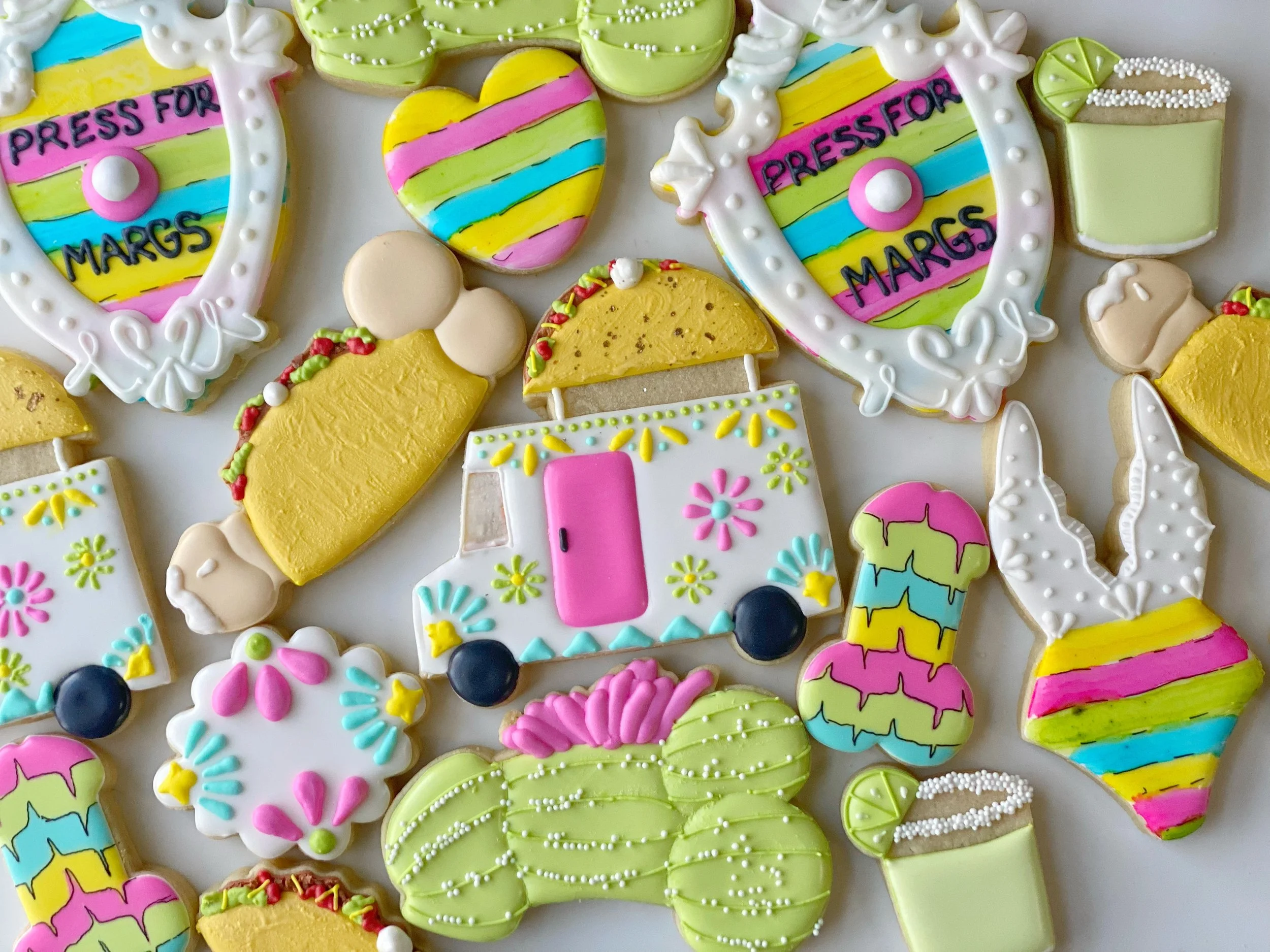 Assorted decorated cookies with various shapes including hearts, camera, ice cream cone, and other designs, decorated with colorful icing and sprinkles.