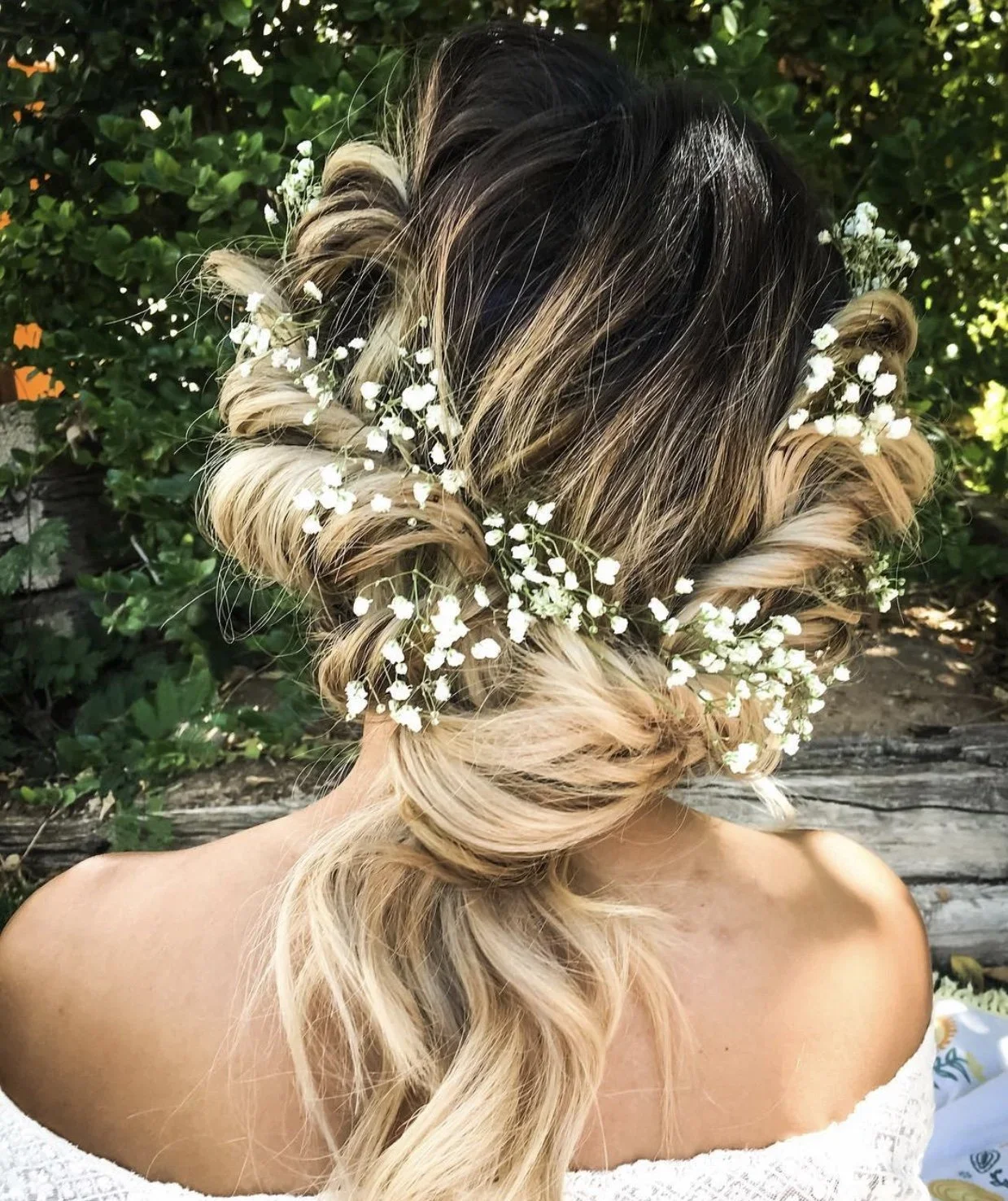 Woman with styled blonde hair adorned with white baby's breath flowers, outdoor setting.