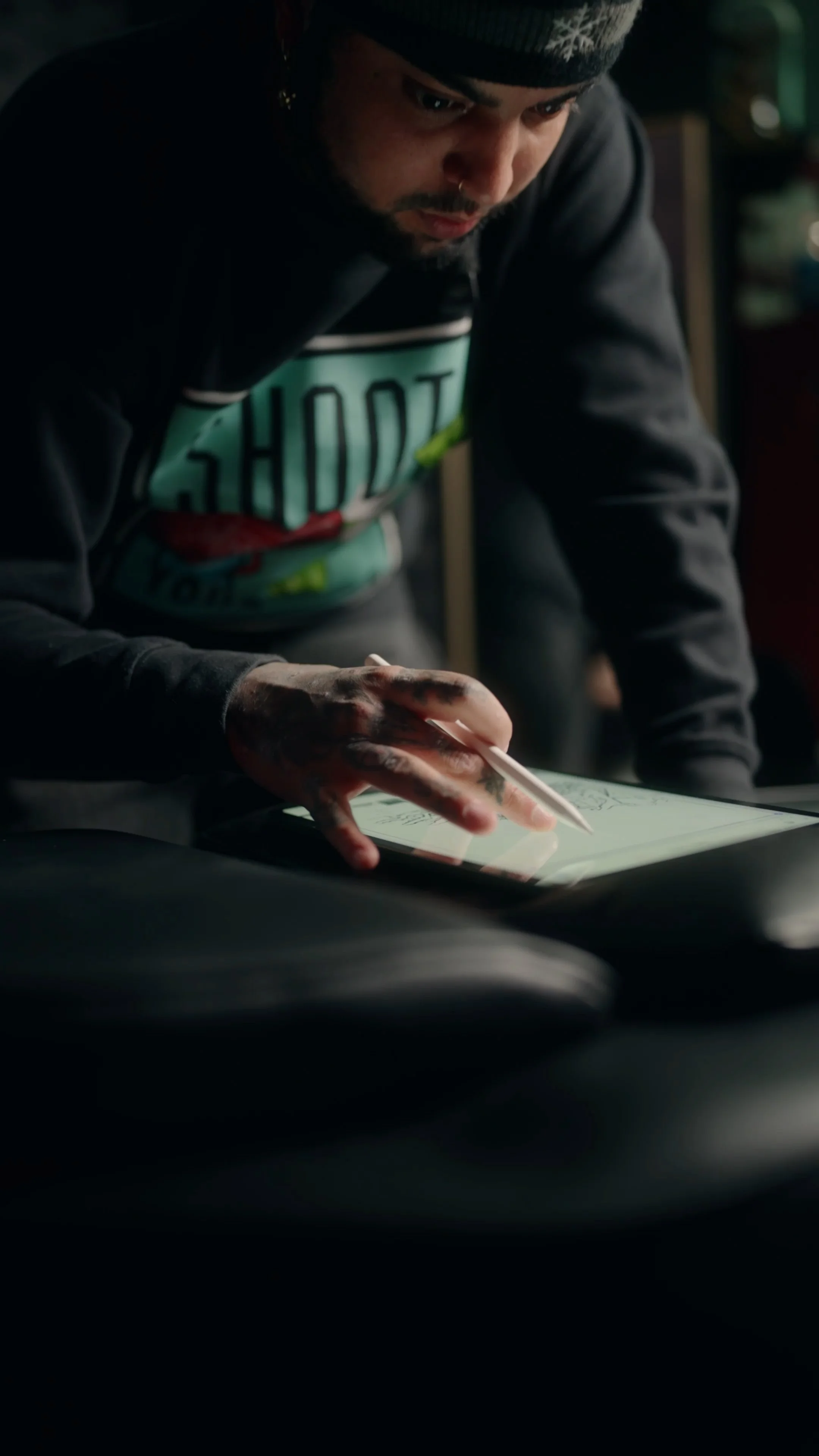 A person using a stylus on a digital tablet in a dimly lit environment.