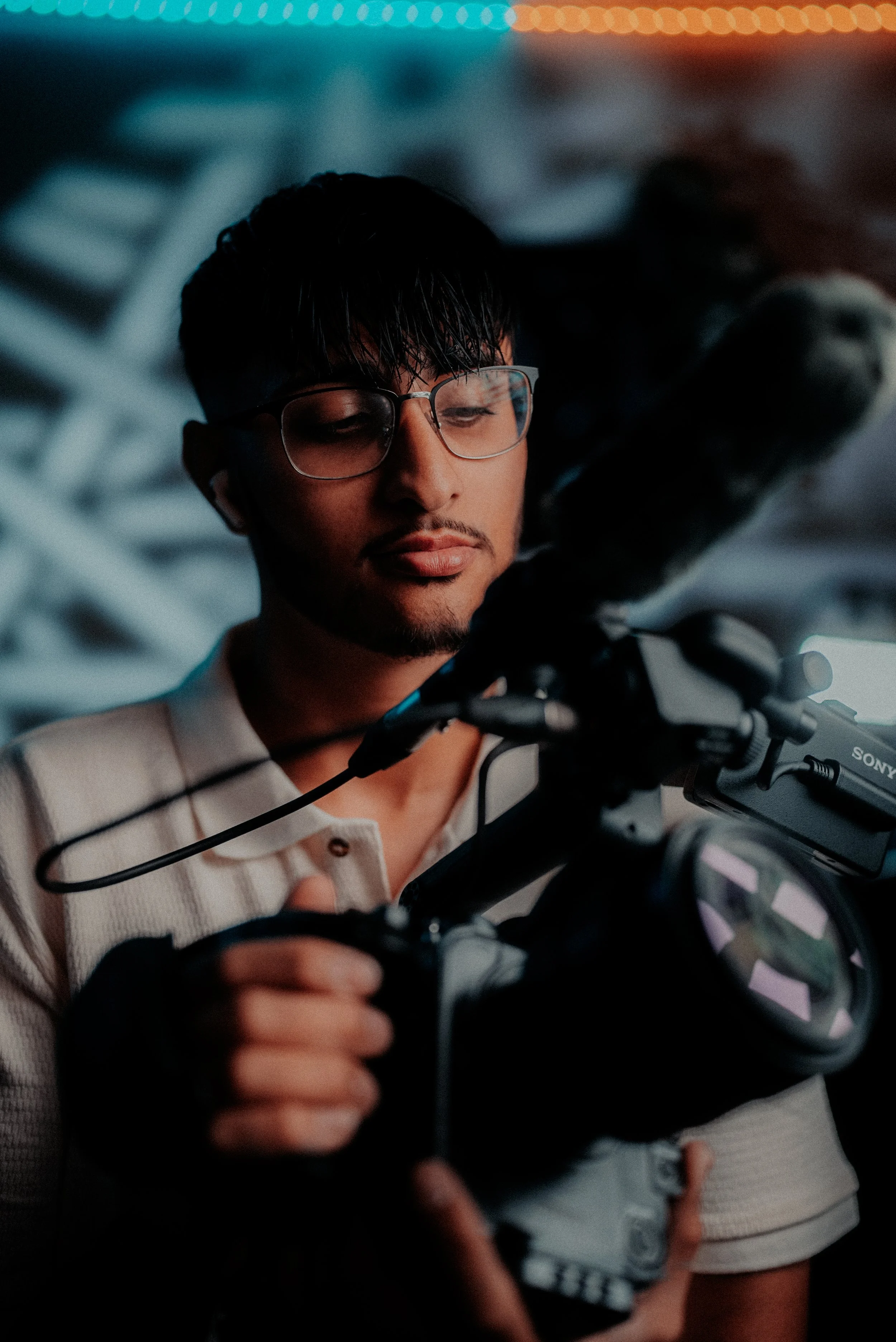 A young man adjusting a professional video camera in a dimly lit environment.