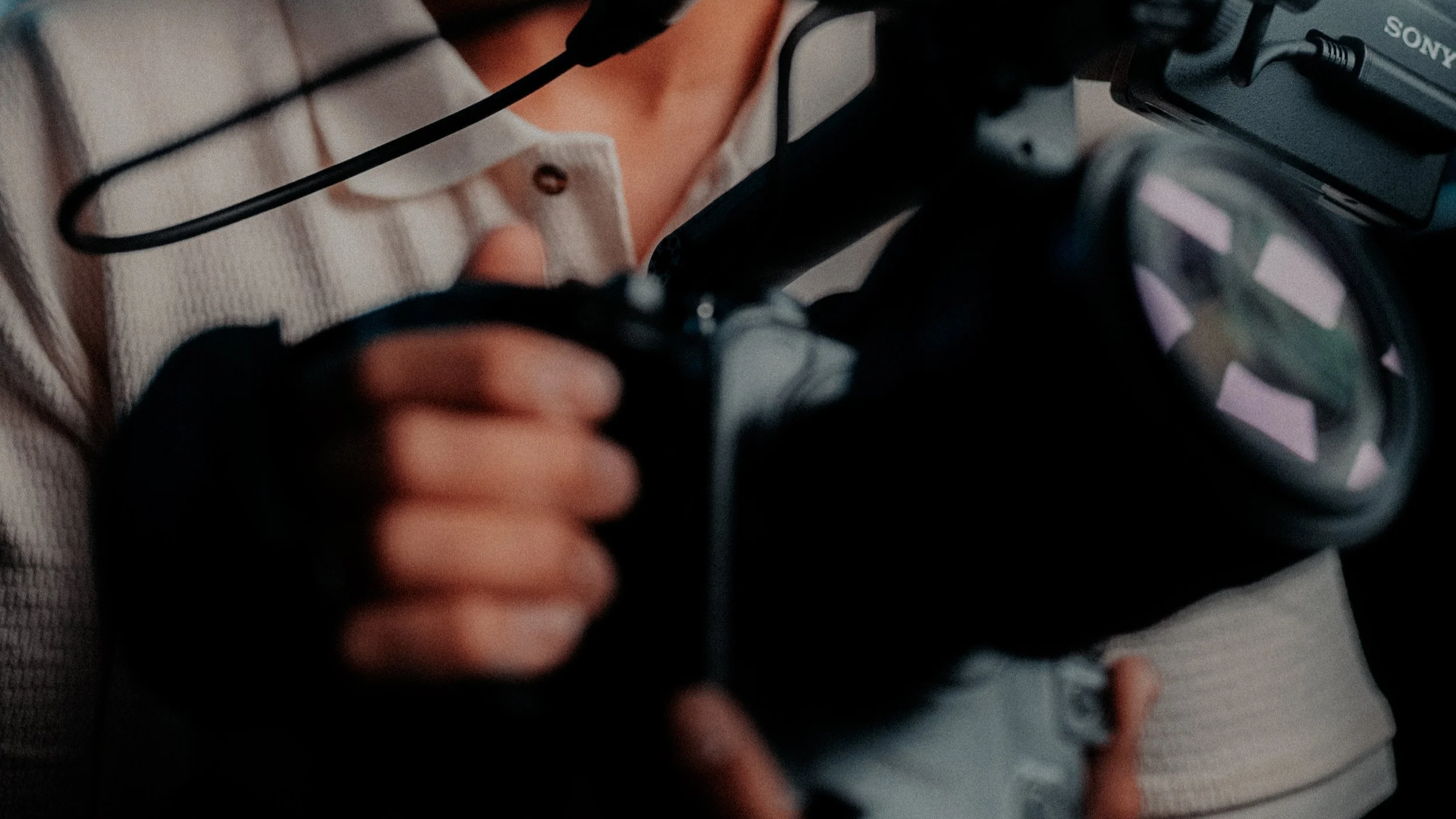 Close-up of a person wearing a white shirt and black gloves, holding a professional camera with an external flash and a viewfinder, while adjusting camera settings.