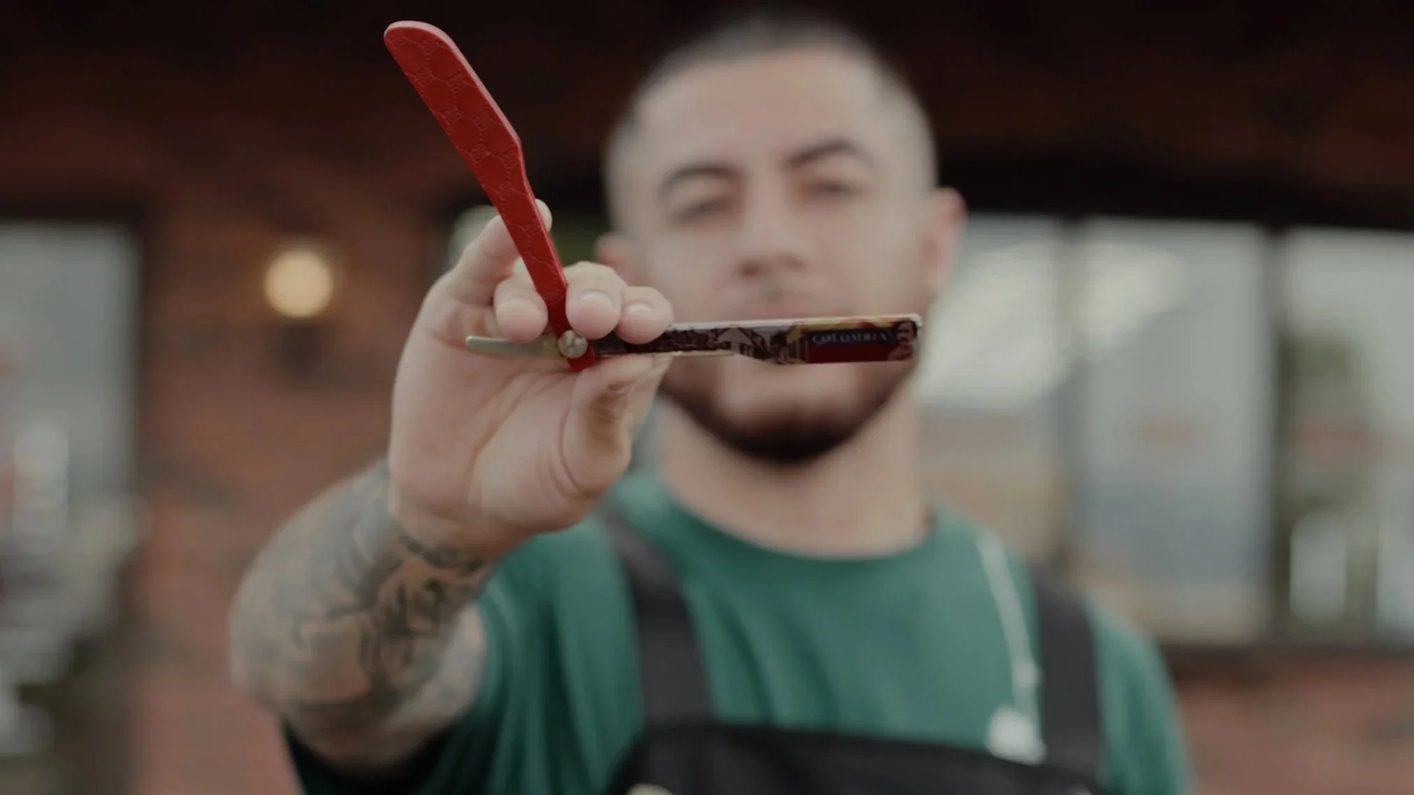A man with tattoos on his arm holding a snooker cue towards the camera, focusing on the cue with a blurred background.
