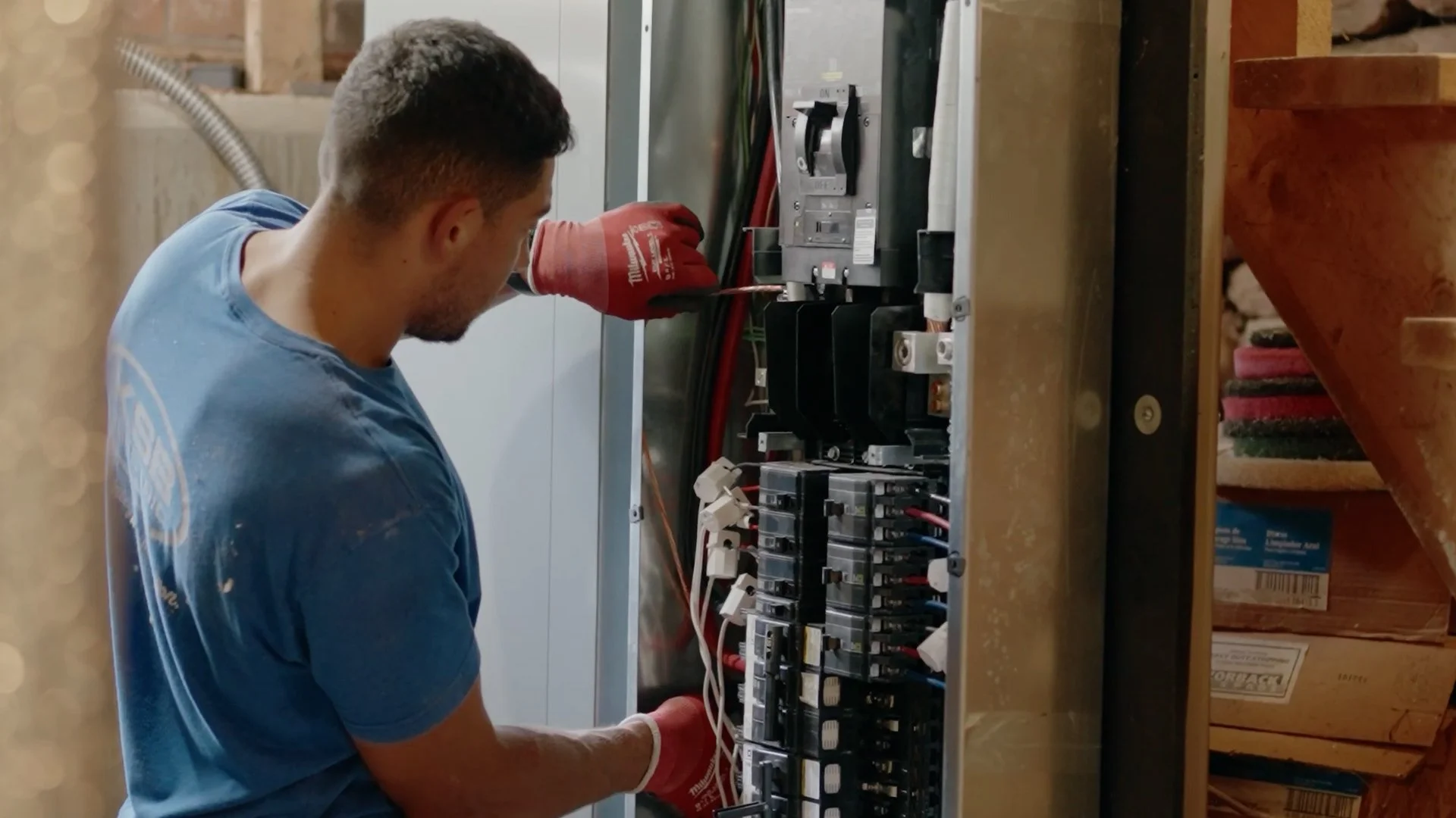 A technician wearing red gloves working on an electrical panel or breaker box.