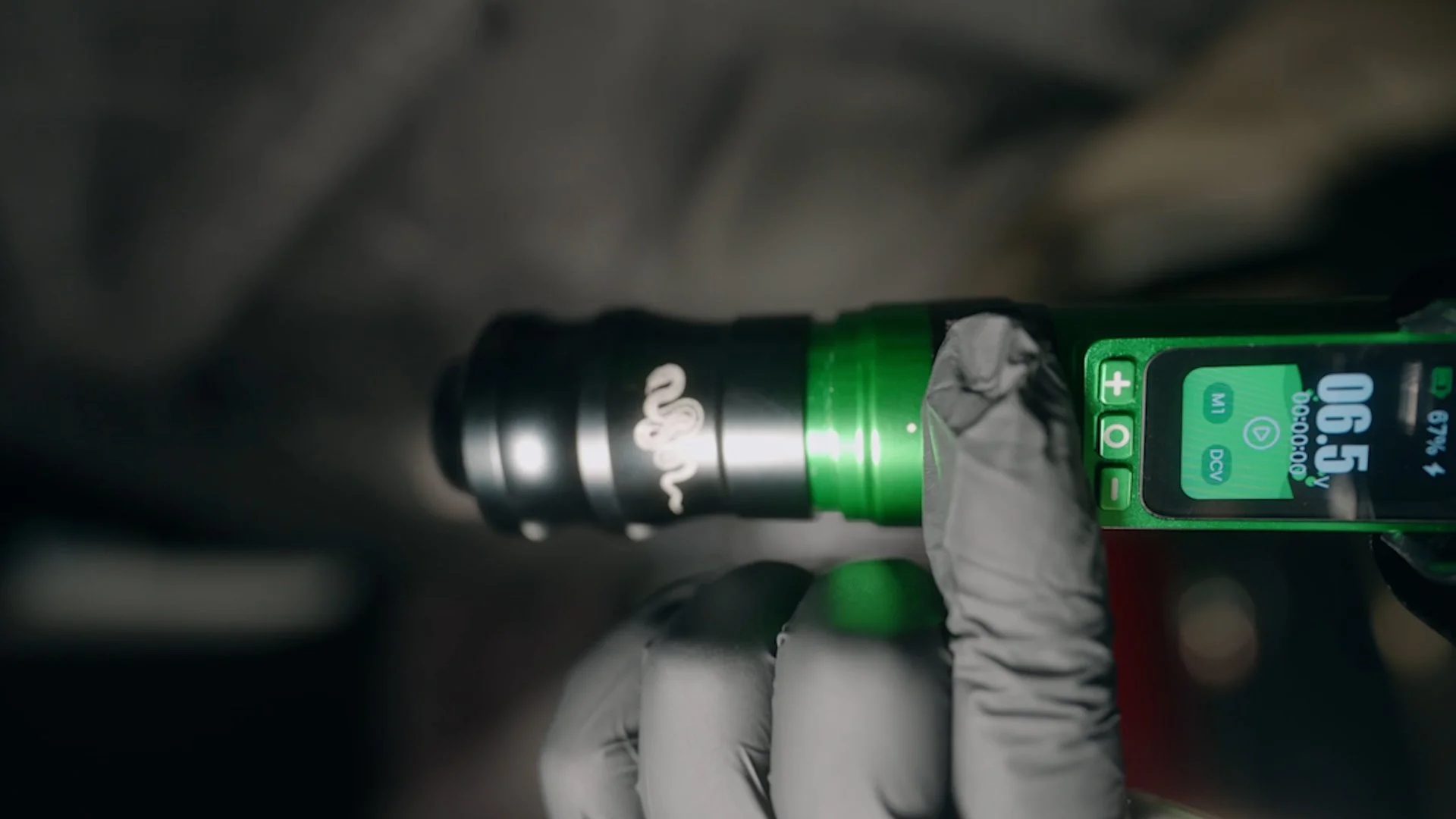 A person wearing gray gloves holds a dosing device with a digital display, producing a beam of bright white light from its tip, with a blurred background.