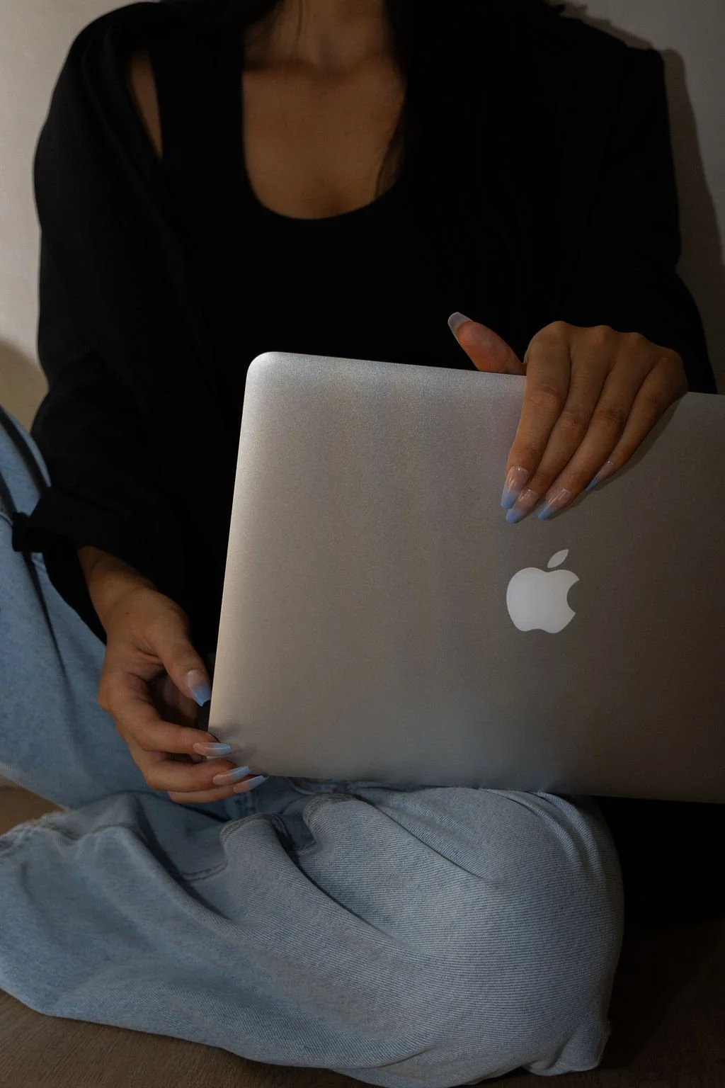 Person sitting on the floor holding a closed silver MacBook laptop.