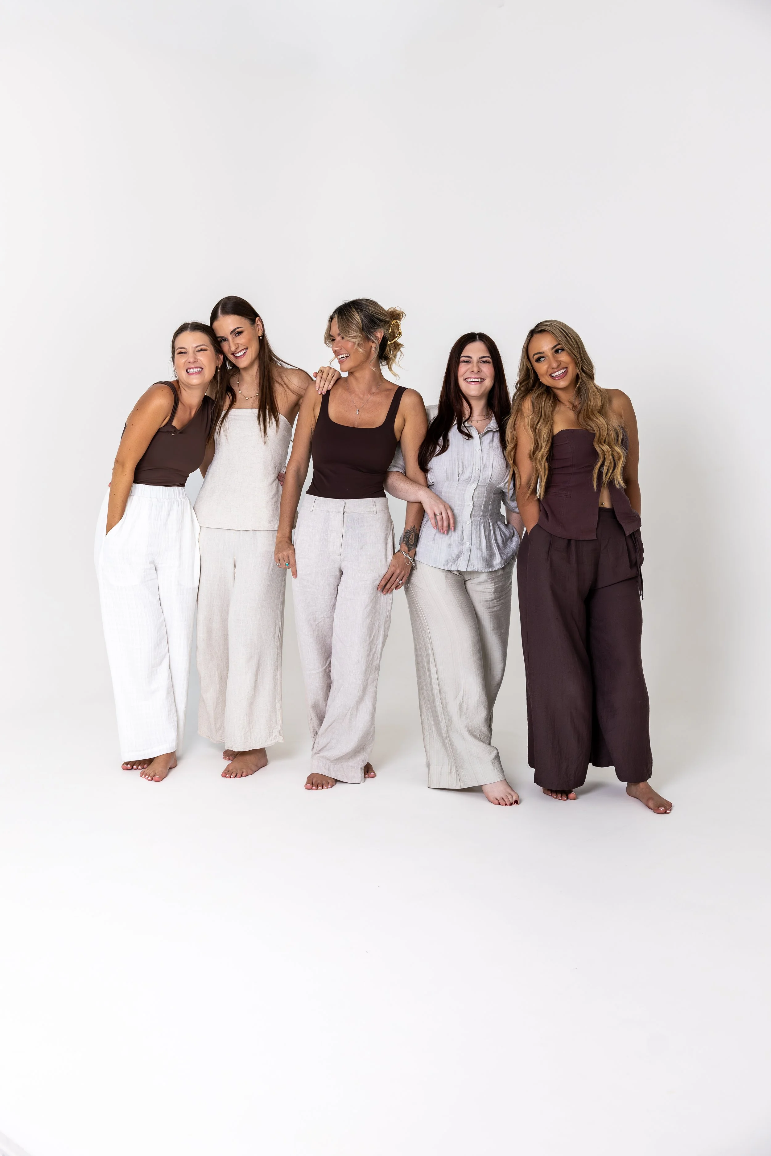 Group of five women standing close together, smiling, in casual clothing, with a plain white background. The team is made up of counsellors, psychologist, psychotherapist, childrens therapy, family therapy.