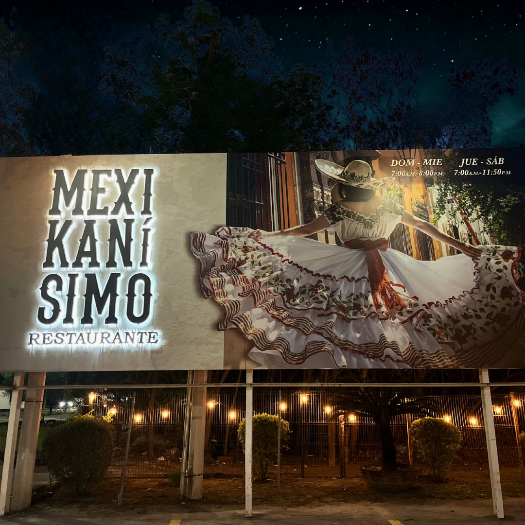 Cartel de restaurante mexicano llamado Mexi Kani Simo con horario de apertura y una figura de una mujer vestida con un vestido folklórico y sombrero, en un fondo nocturno con árboles y luces.