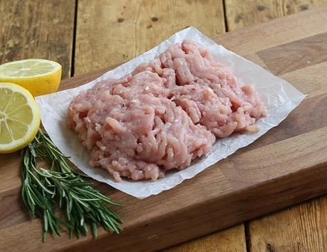 Raw ground chicken on parchment paper on a wooden cutting board with lemon wedges and rosemary.