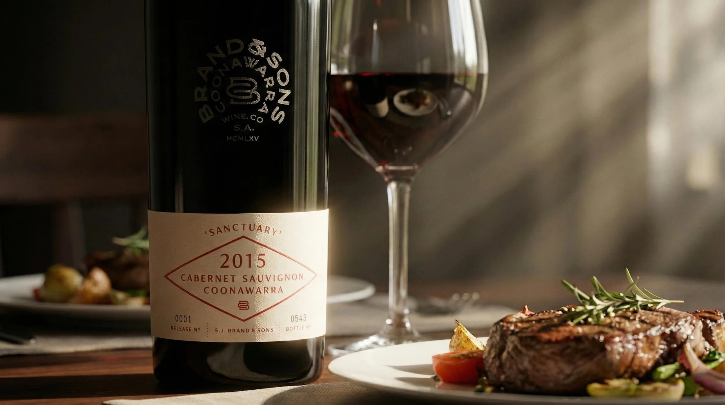 A bottle of Sanctorium Cabernet Sauvignon 2015 wine next to a glass of red wine, with a plate of food and some herbs in the background and foreground.