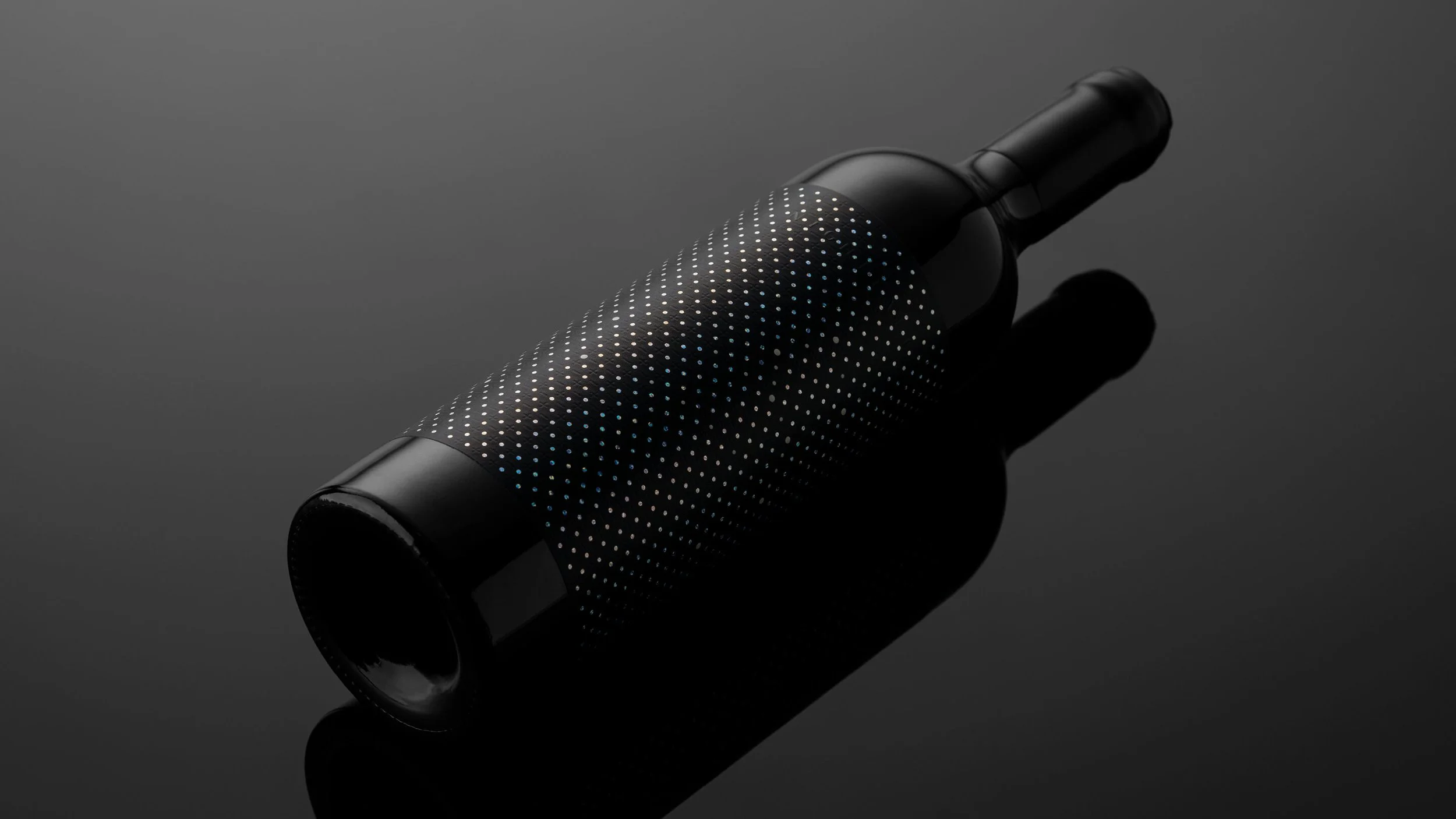 A black wine bottle wrapped with a textured, dotted sleeve on a reflective black surface.