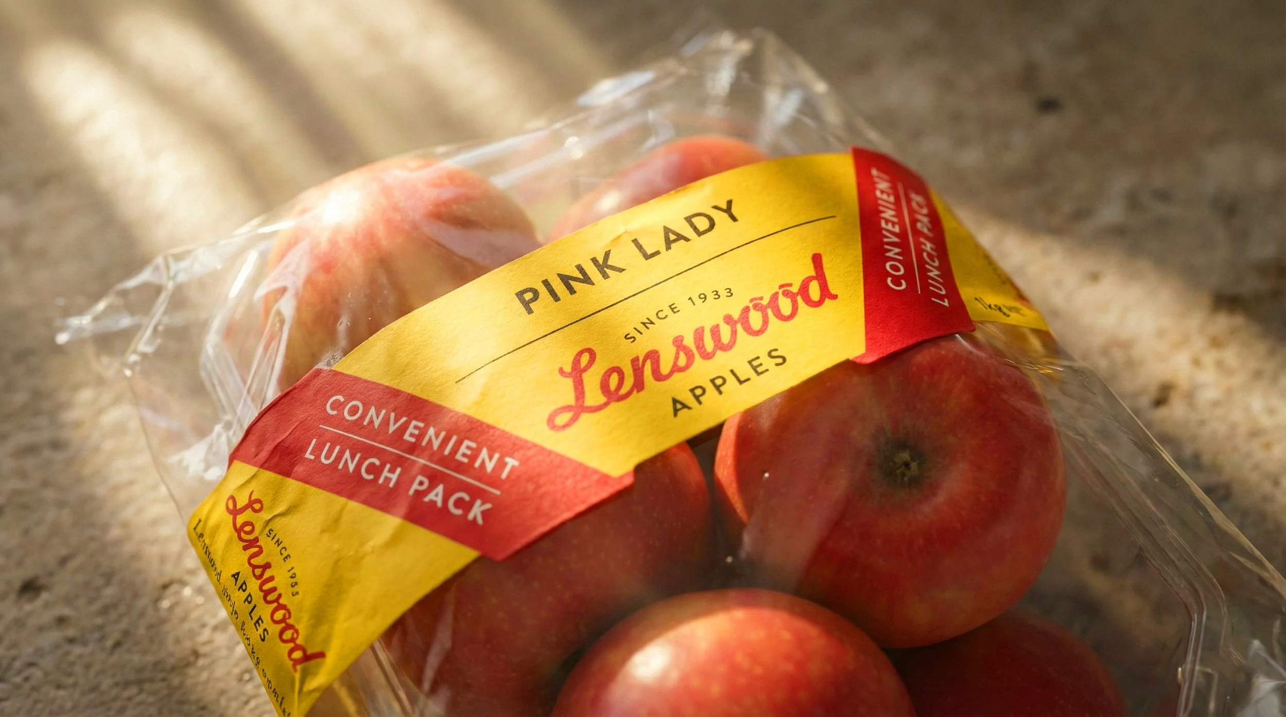 A plastic container of Pink Lady apples with a yellow and red label reading 'Lenswood Apples', 'Convenient Lunch Pack', on a kitchen countertop.