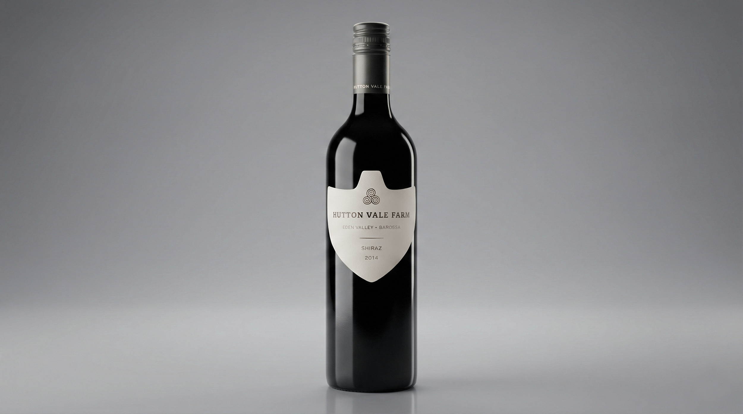 A dark glass bottle of Hutton Vale Farm Shiraz wine from 2014 on a gray background.