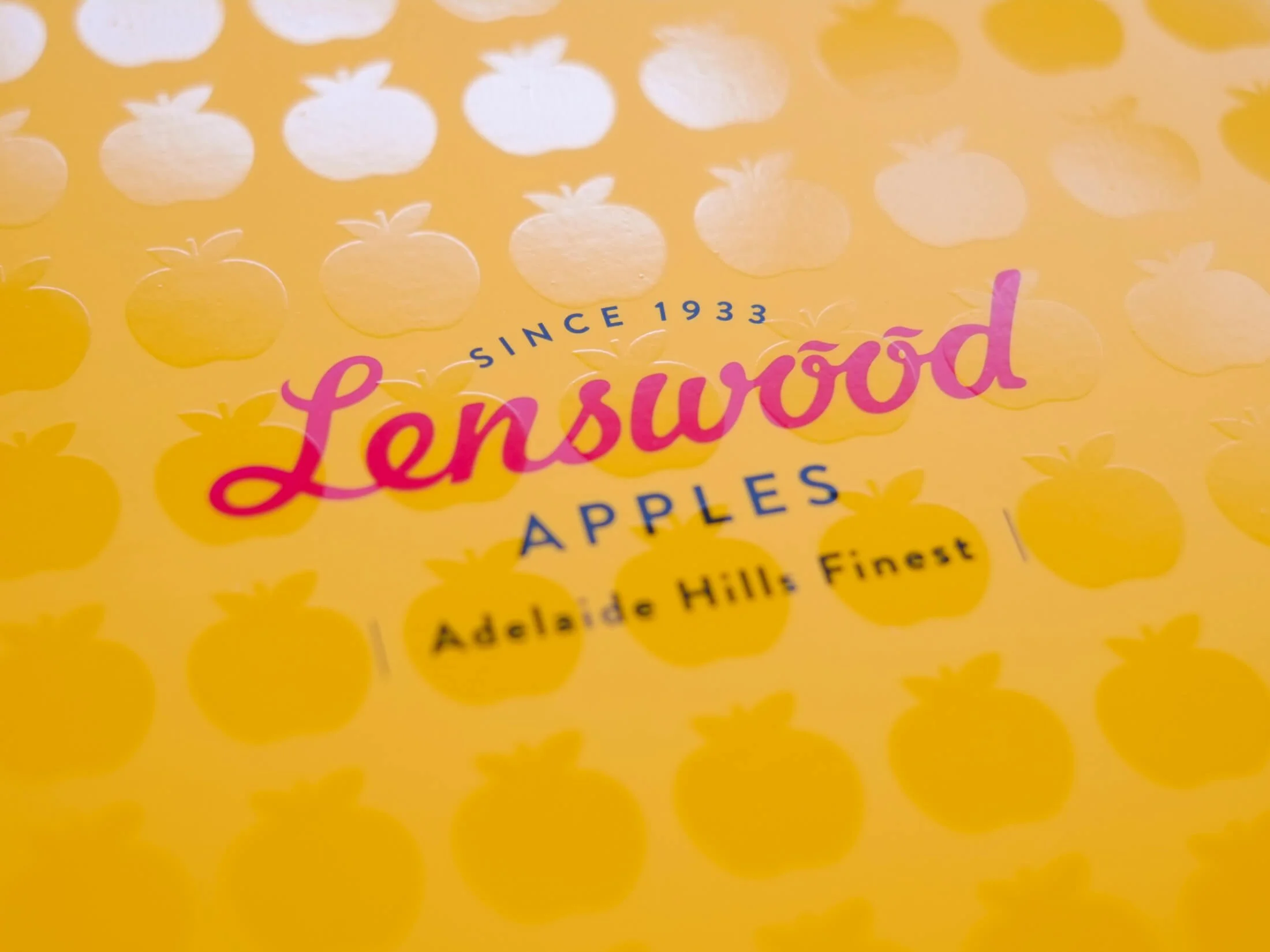 Bright yellow packaging with a pattern of white and yellow apples. The brand name 'Lentswood' is written in pink, with the words 'Since 1933' above and 'Apples' below in blue. The label also states 'Adelaide Hills Finest' in black.