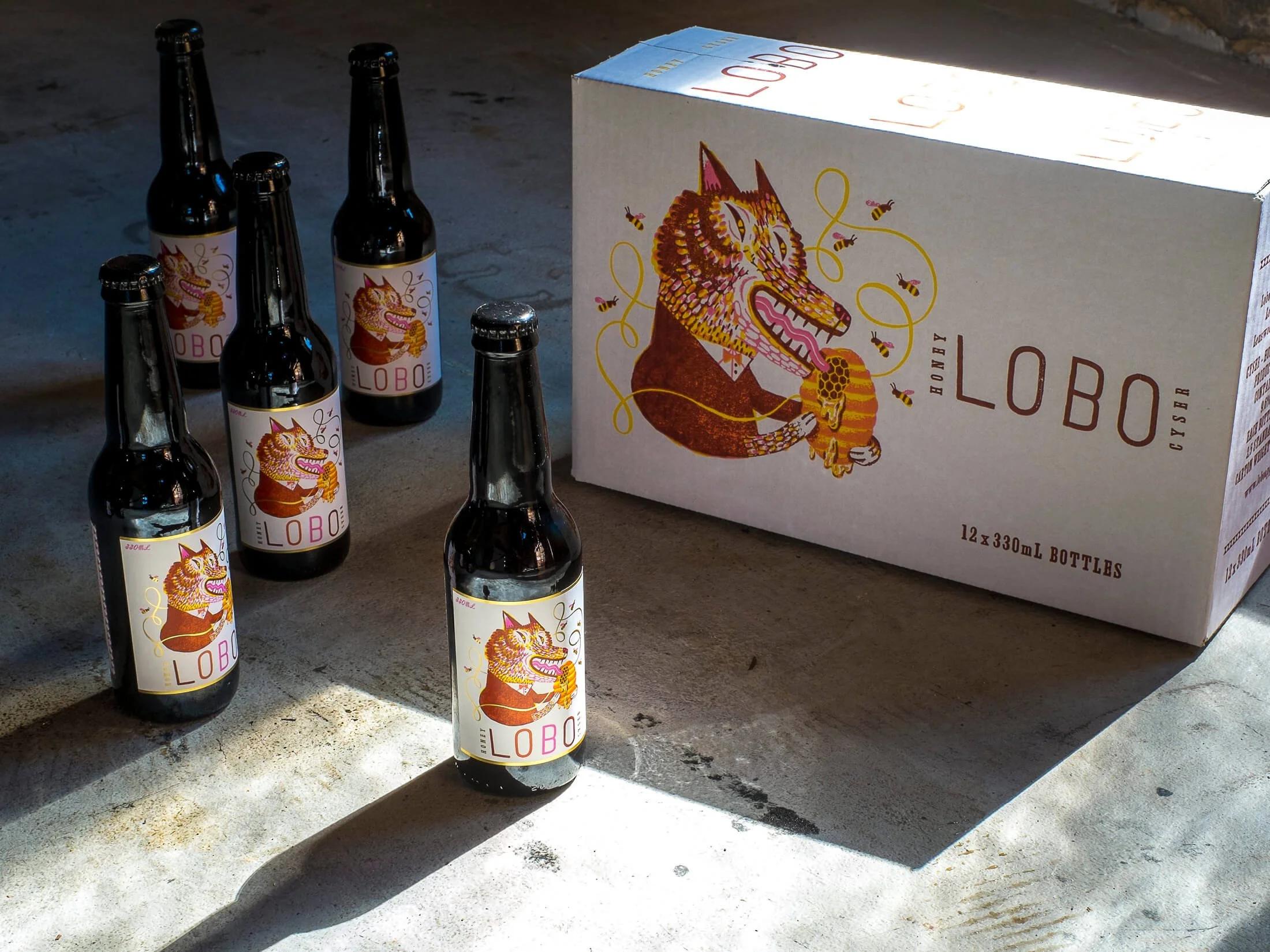 A box of Lobo honey bottles and six individual honey bottles with cartoon wolf labels on a concrete surface.