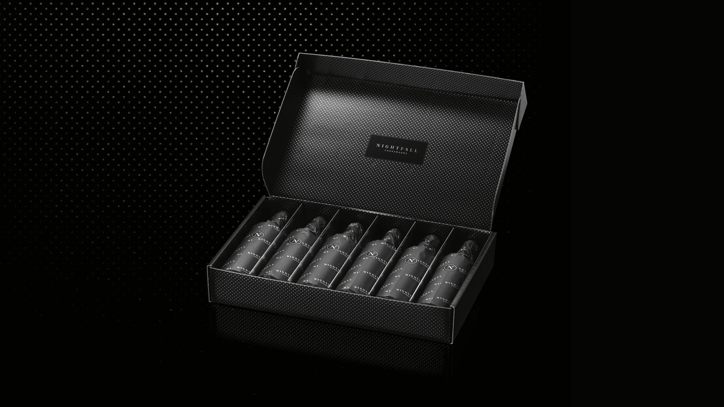 Open black box containing six vials labeled Nightfall against a black dotted background.