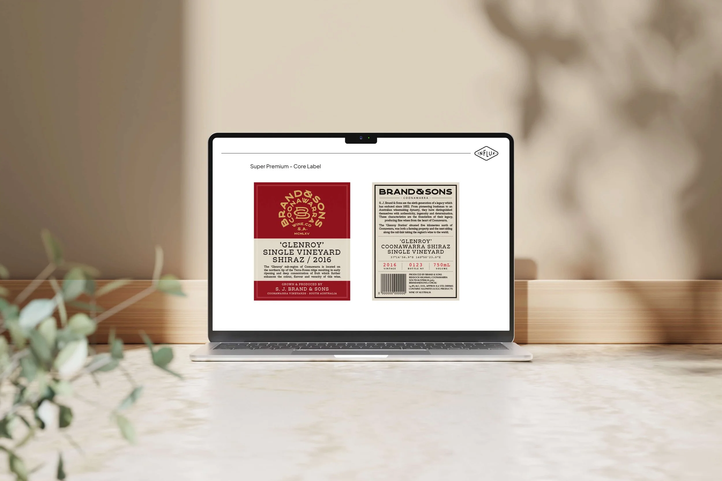 Laptop displaying wine bottle labels with branding and wine details on a wooden desk