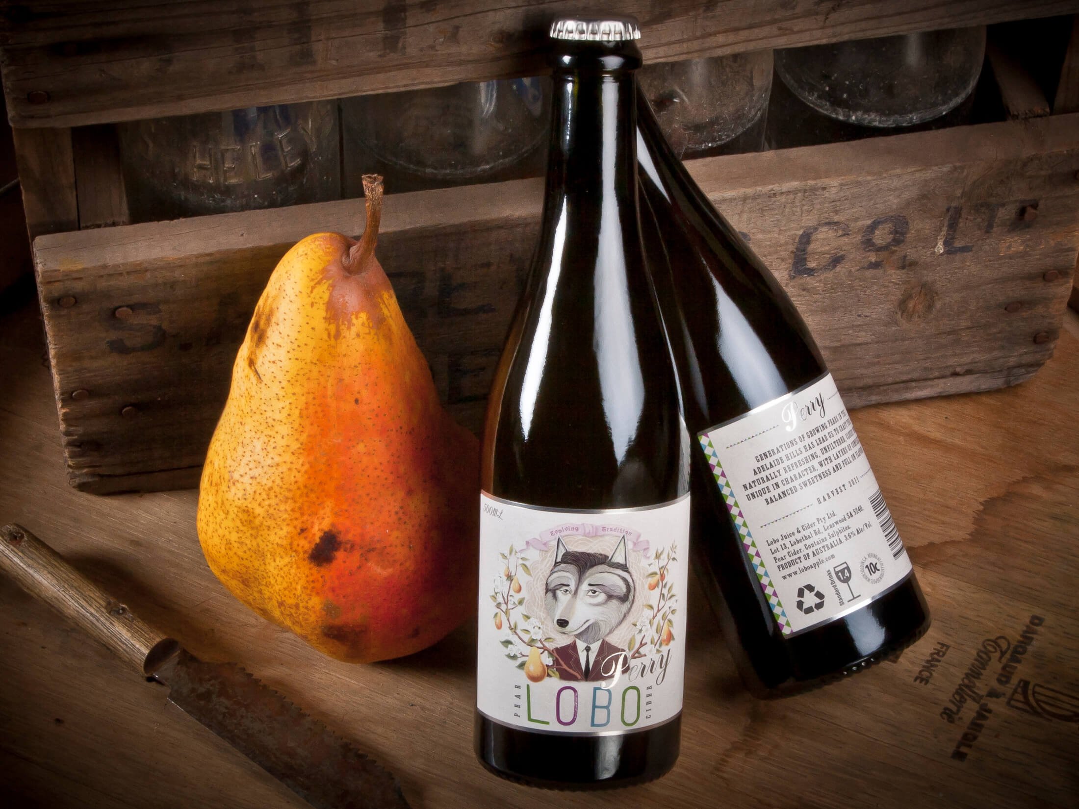 A pear and a bottle of cider on a wooden surface with a wooden crate in the background.