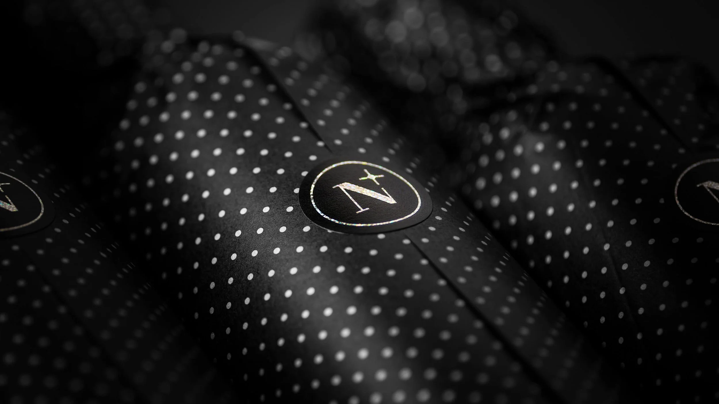 Close-up of black tissue wrapped packaging with white polka dots and a circular logo with the letter 'N' and 'X' on it for Nightfall Wines bottles.