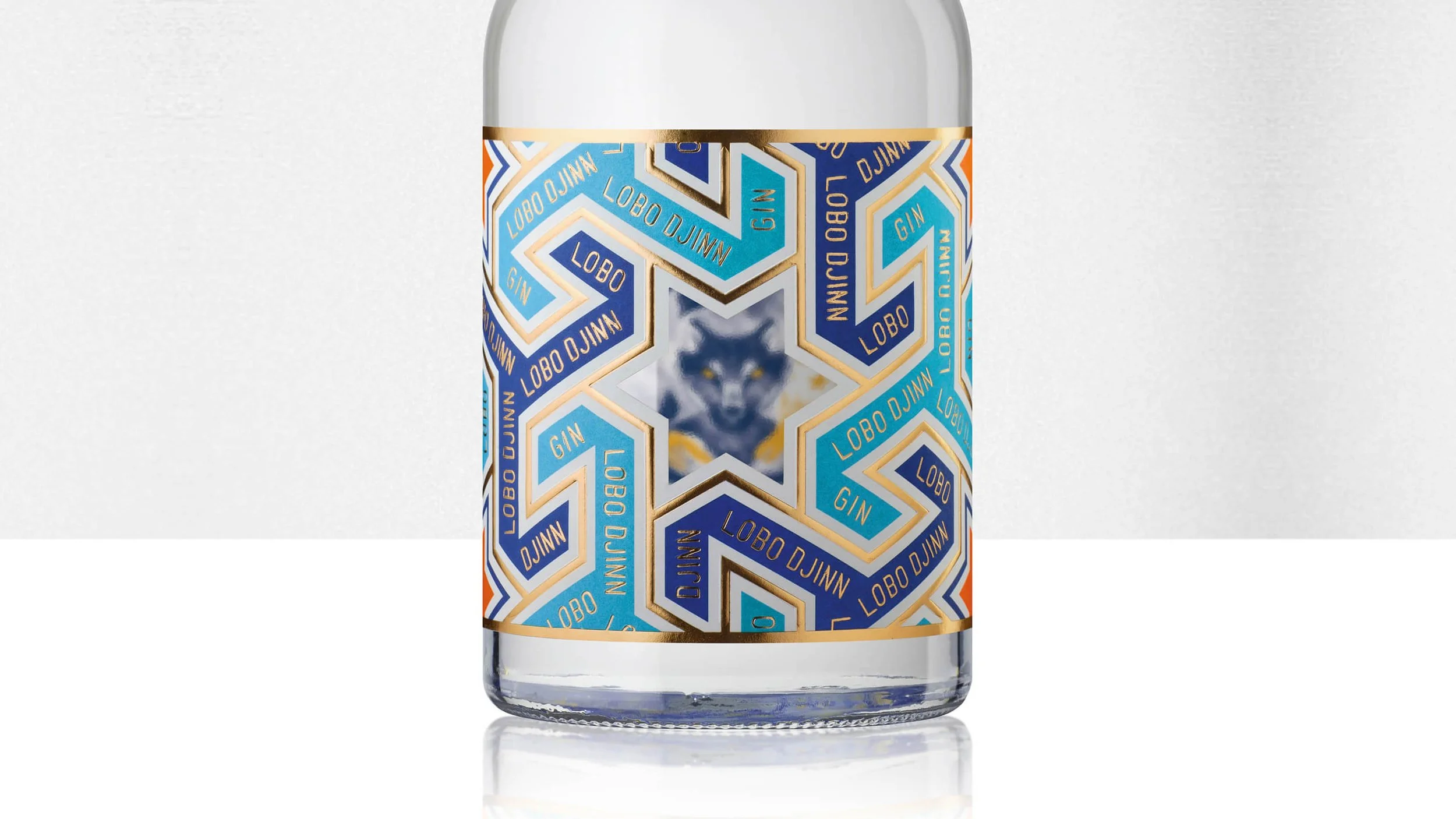A clear glass bottle with a colorful geometric label featuring the words "LOBO DJINN" and "GIN" in blue, white, and gold, with a central image of a wolf's face.