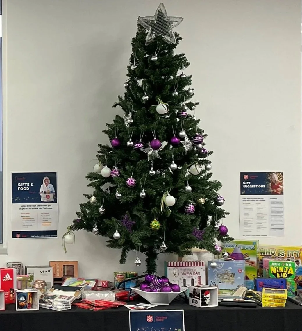 Christmas tree decorated with silver, purple, and white ornaments, topped with a star, and surrounded by toys and gifts on a table.