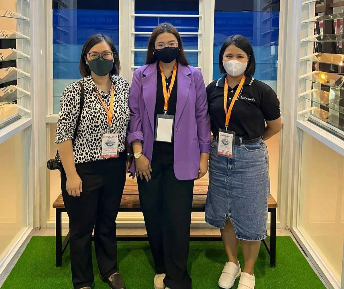 Three women wearing face masks and conference badges standing inside a booth at a trade show or exhibition.