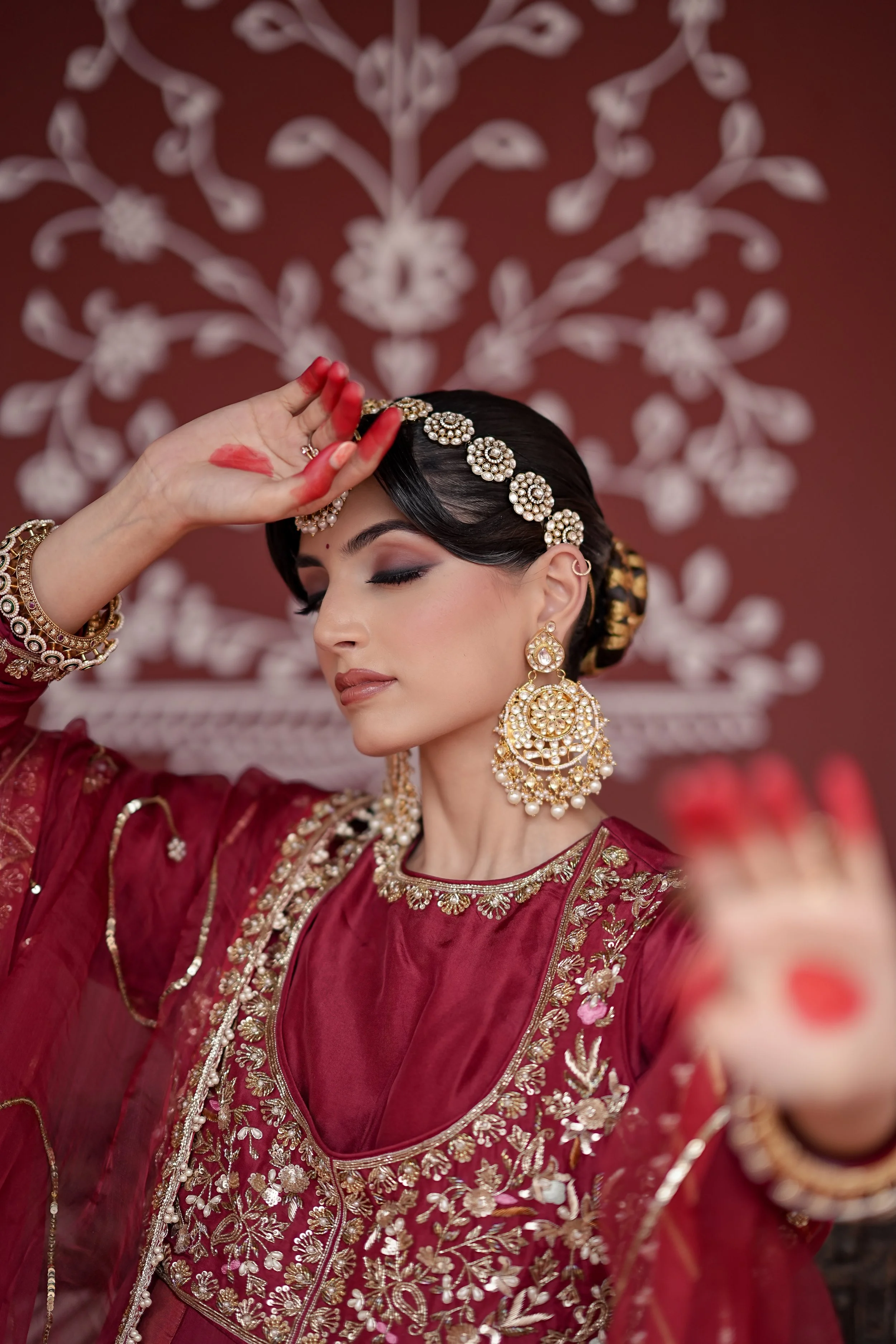 A woman dressed in traditional Indian attire, wearing ornate jewelry, and applying henna on her hand.