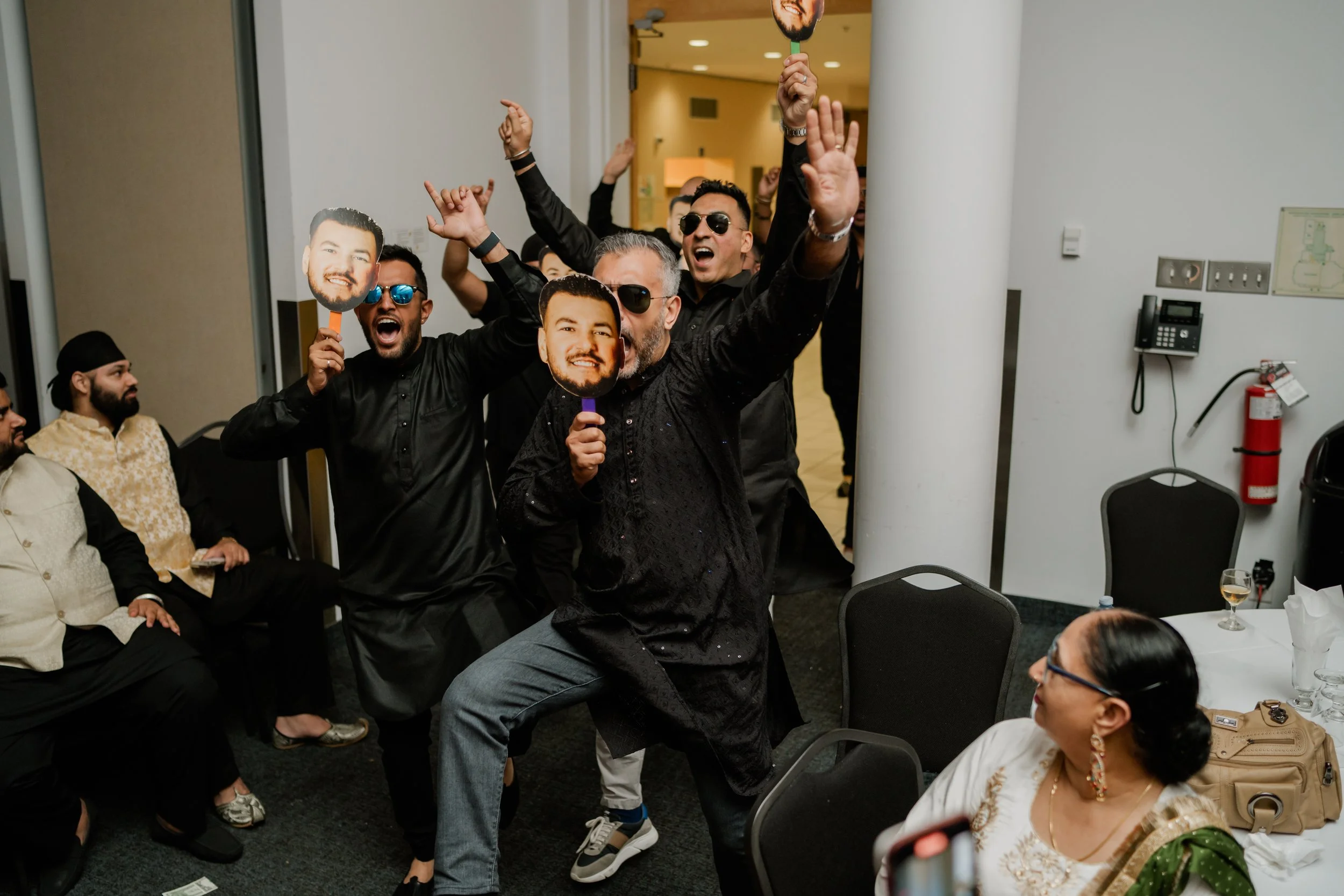 Group of celebration attendees, some holding cutouts of a man's face, dancing and cheering at an indoor event.