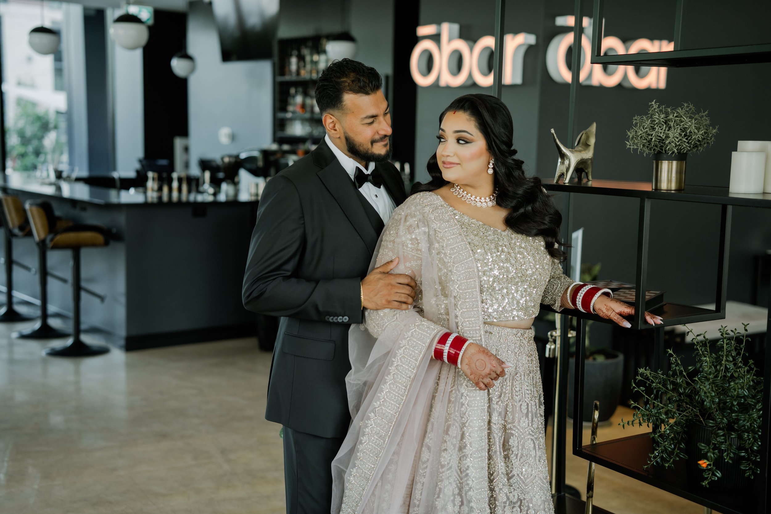 A couple dressed in traditional and formal attire stands inside a modern cafe, enjoying a romantic moment.