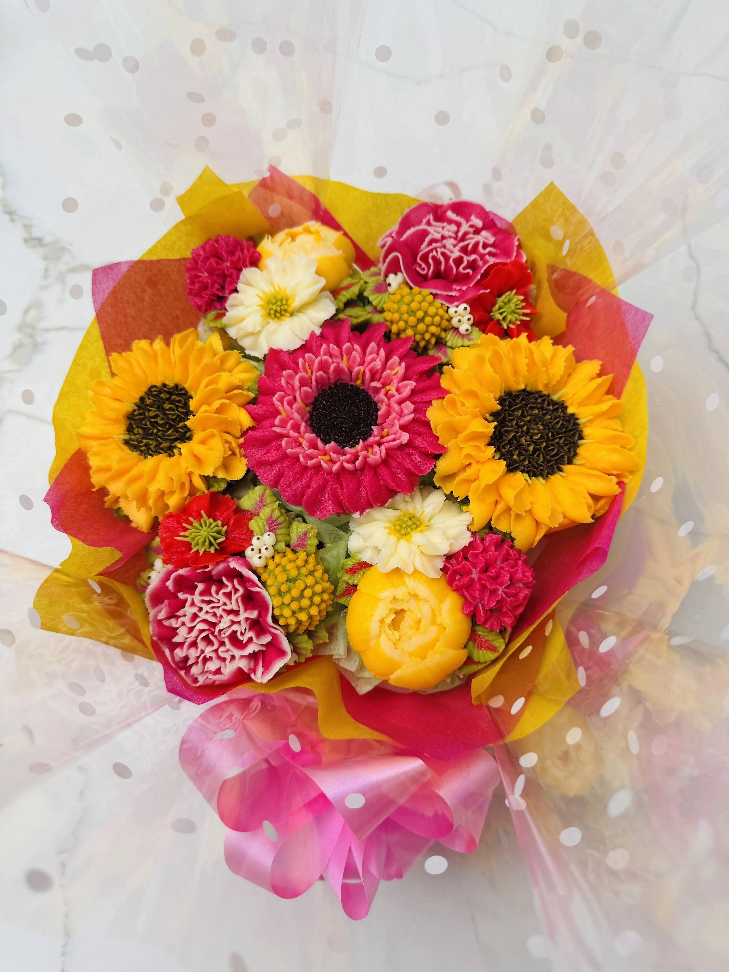 Colorful bouquet of flower cupcakes wrapped in pink and yellow paper with transparent polka dot wrapping.