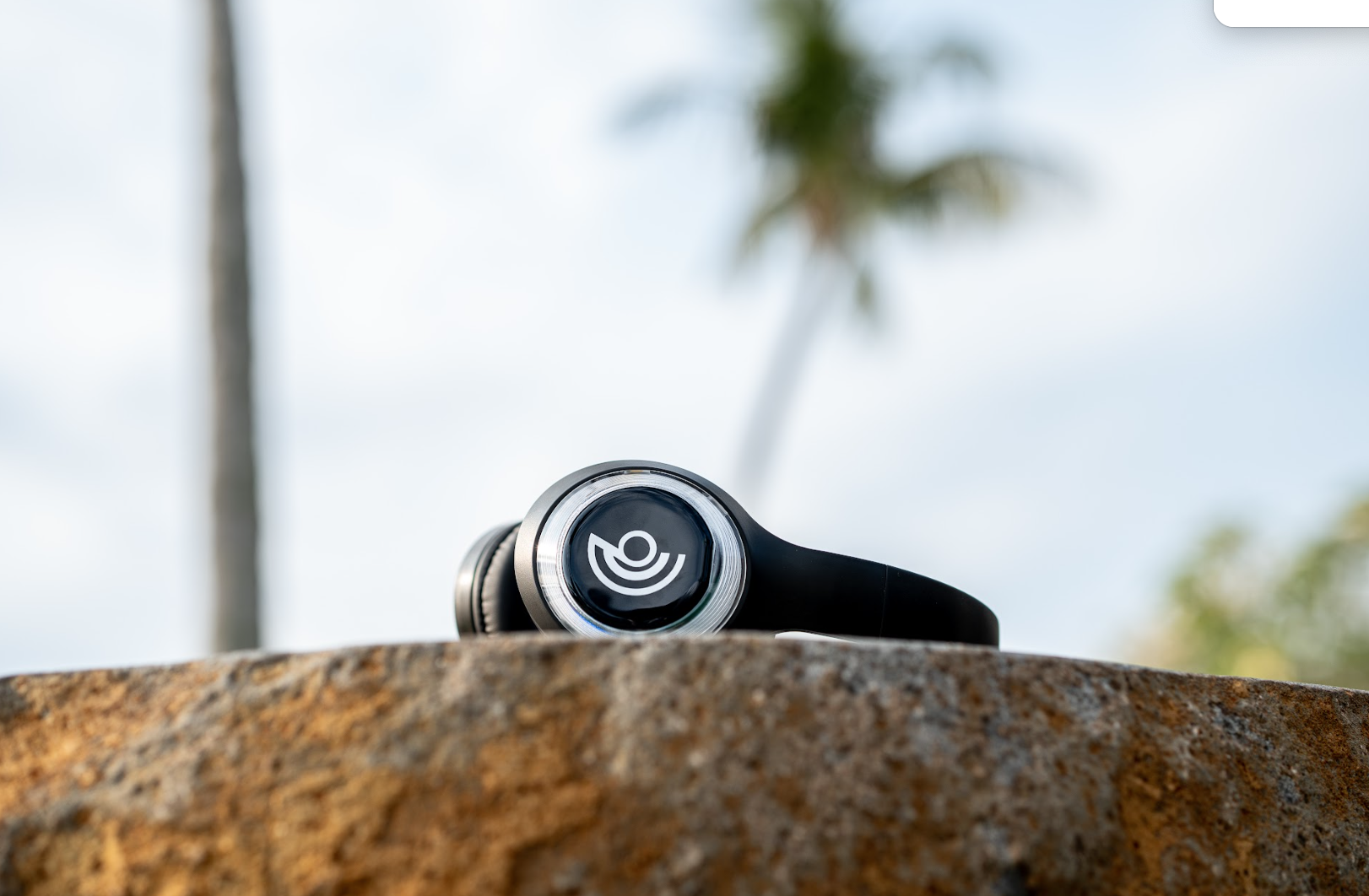 9D Breathwork headphones resting on a stone surface, with palm trees and a cloudy sky in the background.