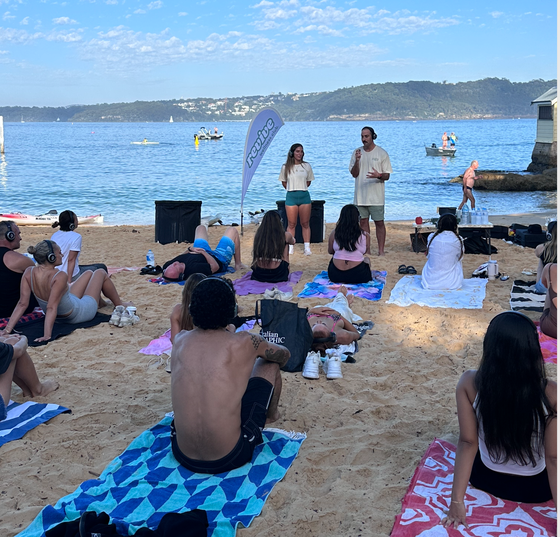 A person standing near the water with arms raised above their head, facing the sea on a cloudy day.