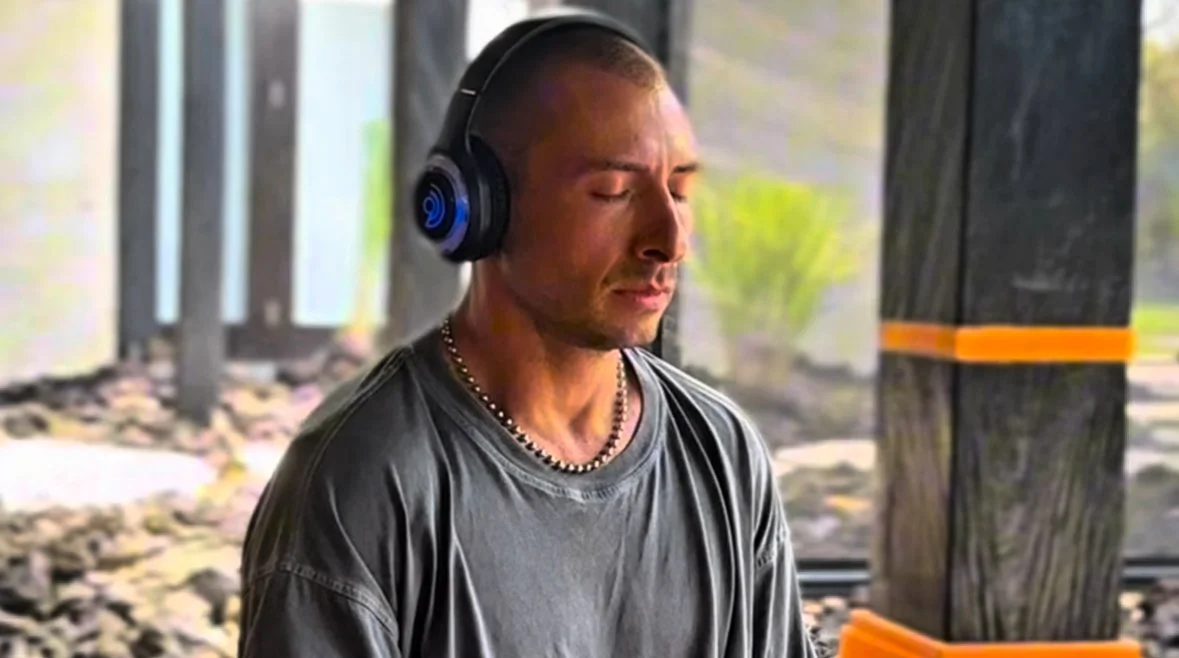 Two people relaxing outdoors on yoga mats by a pool, wearing eye masks and headphones, sunbathing on a sunny day.