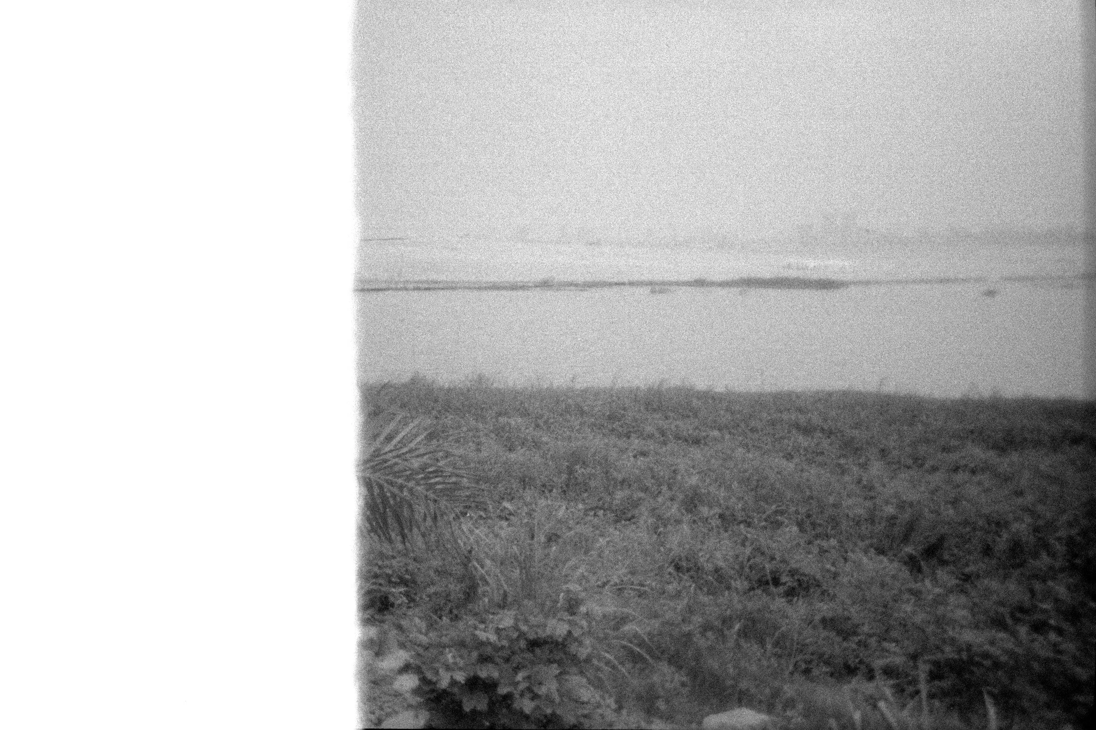 A black and white photo of a beach with a sunset or sunrise, with calm water and a distant shoreline.