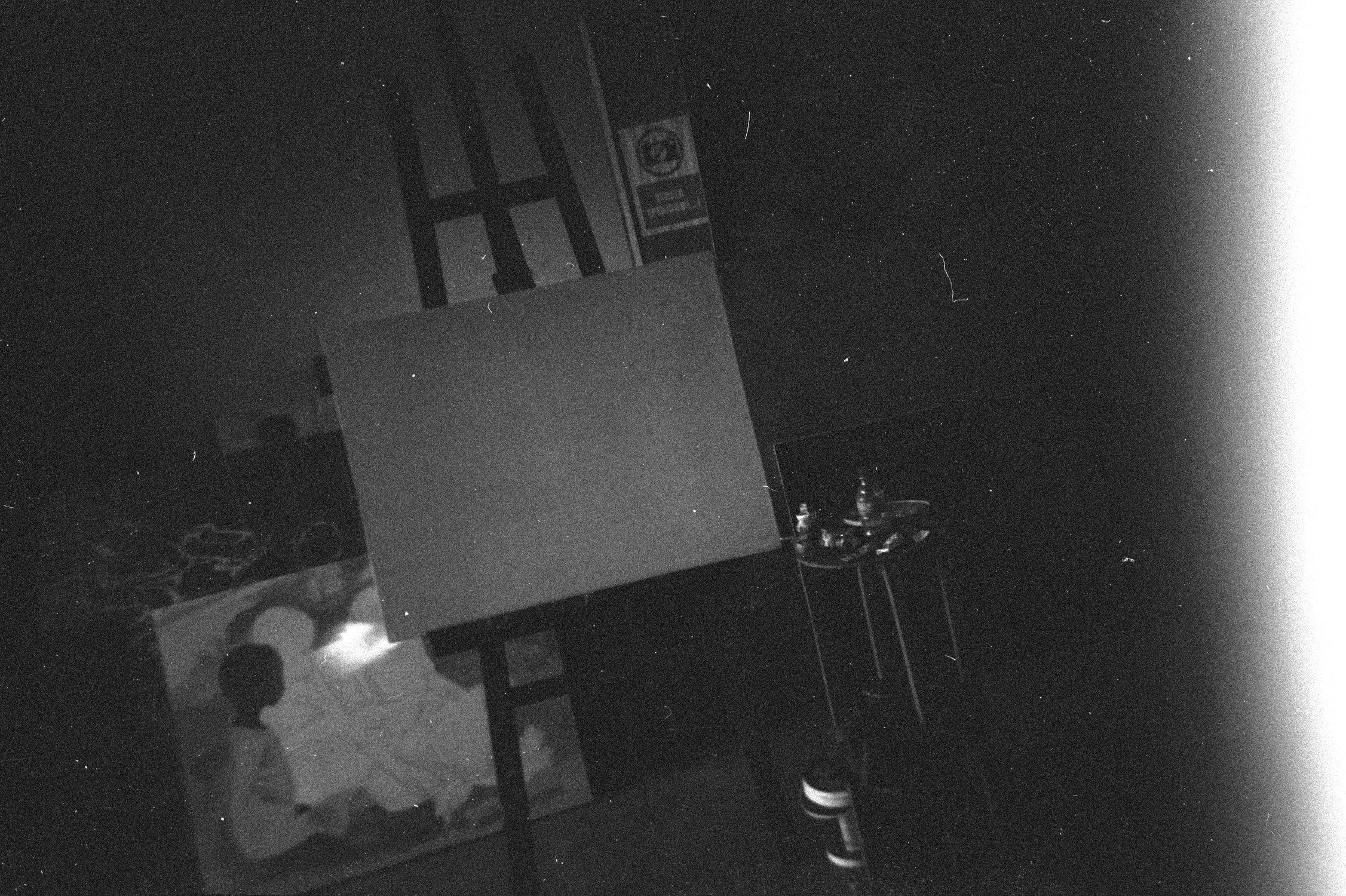 Black and white photo of a dark room with an empty painting canvas.