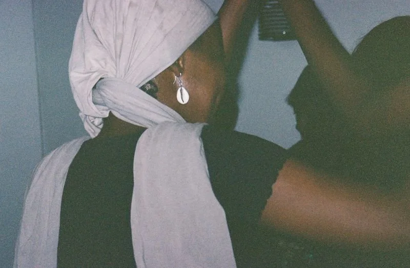 A woman wearing large earrings and a white headscarf in a dark indoor space.