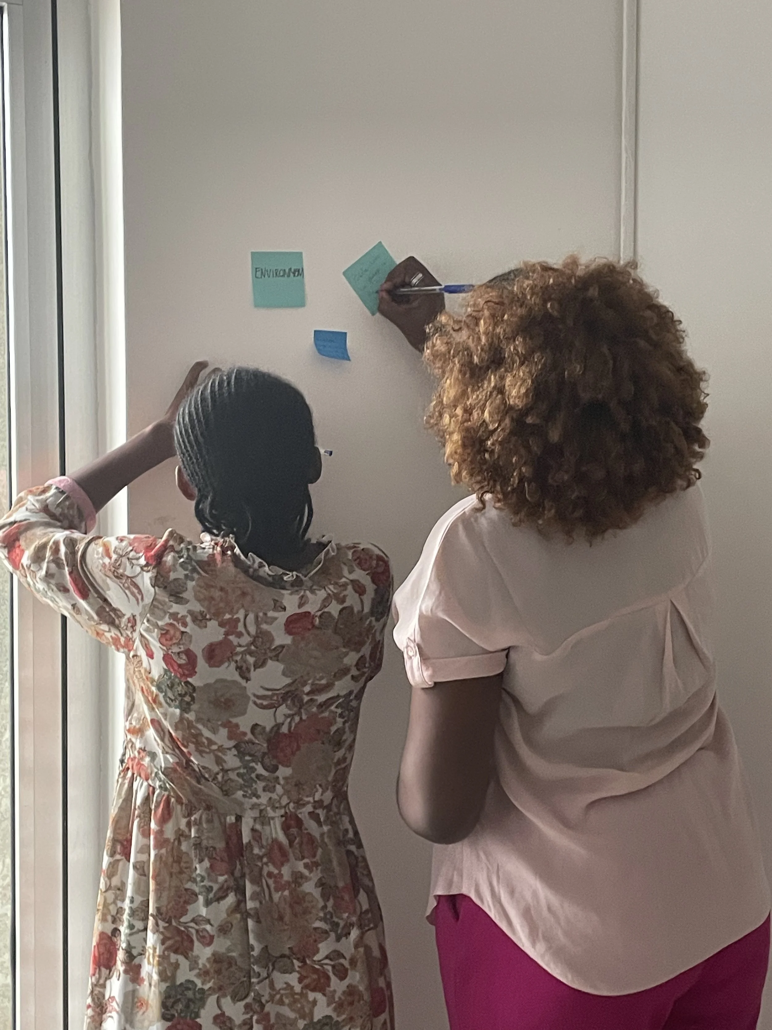Two women writing sticky notes on a wall.