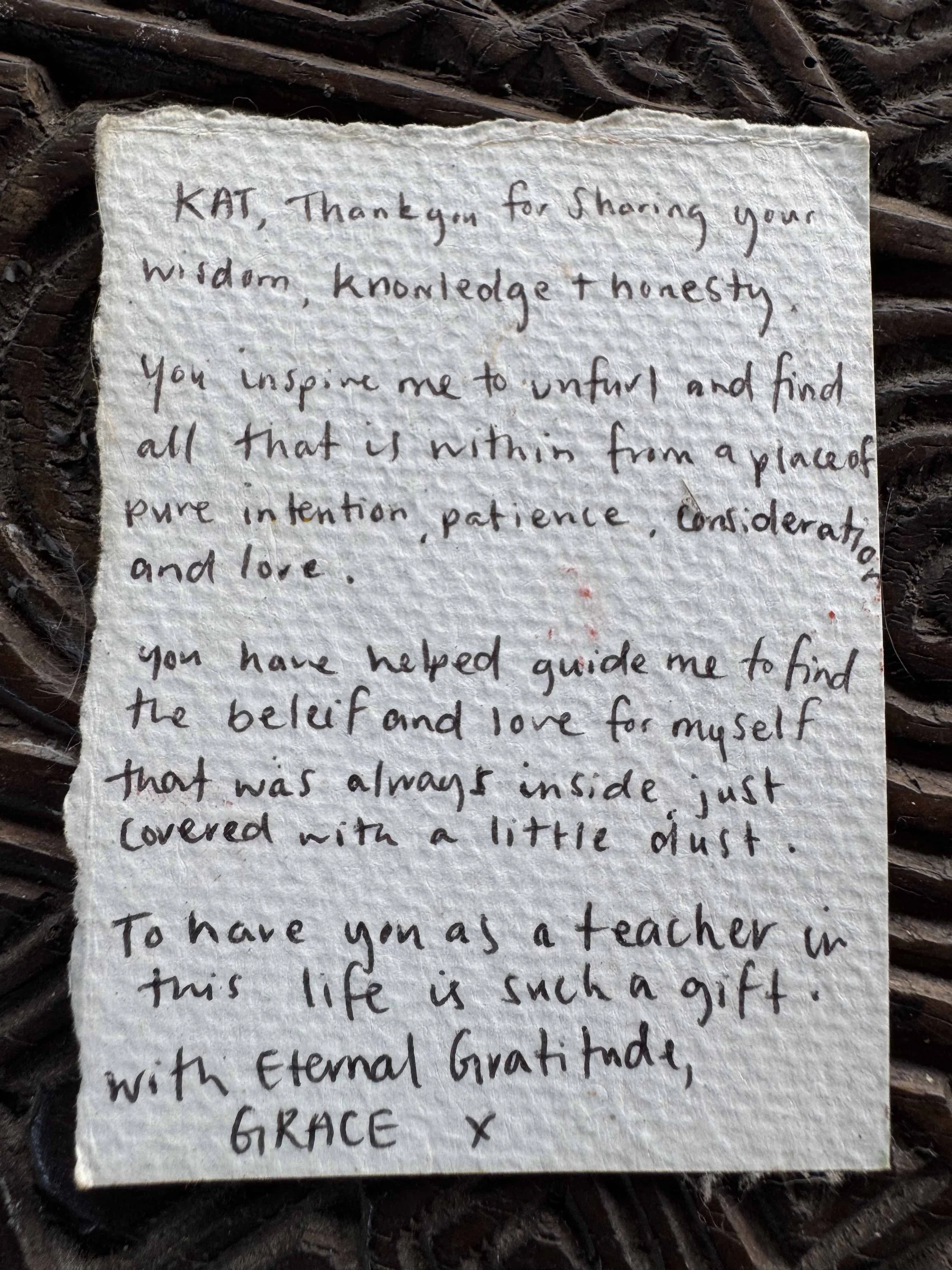 A handwritten note on textured paper, placed on a dark, crinkled surface, with some words partially visible. The note expresses gratitude and mentions sharing wisdom, love, guidance, and a gift called life.
