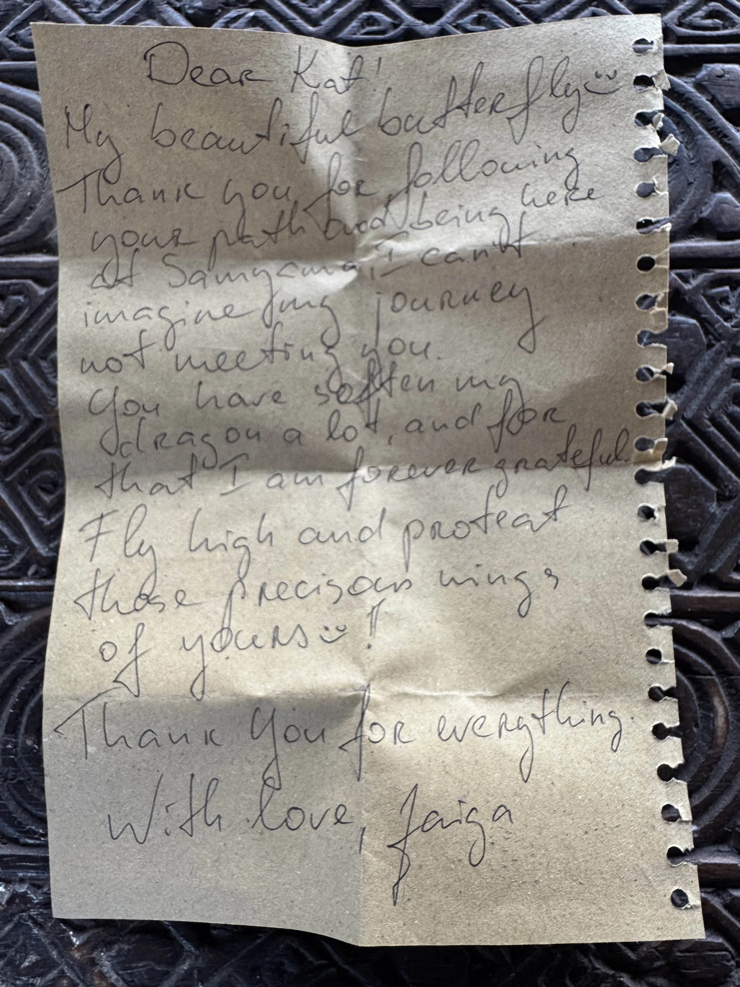 A handwritten thank you letter on torn, beige notebook paper with wire-bound holes on the right side, placed on a textured black surface.