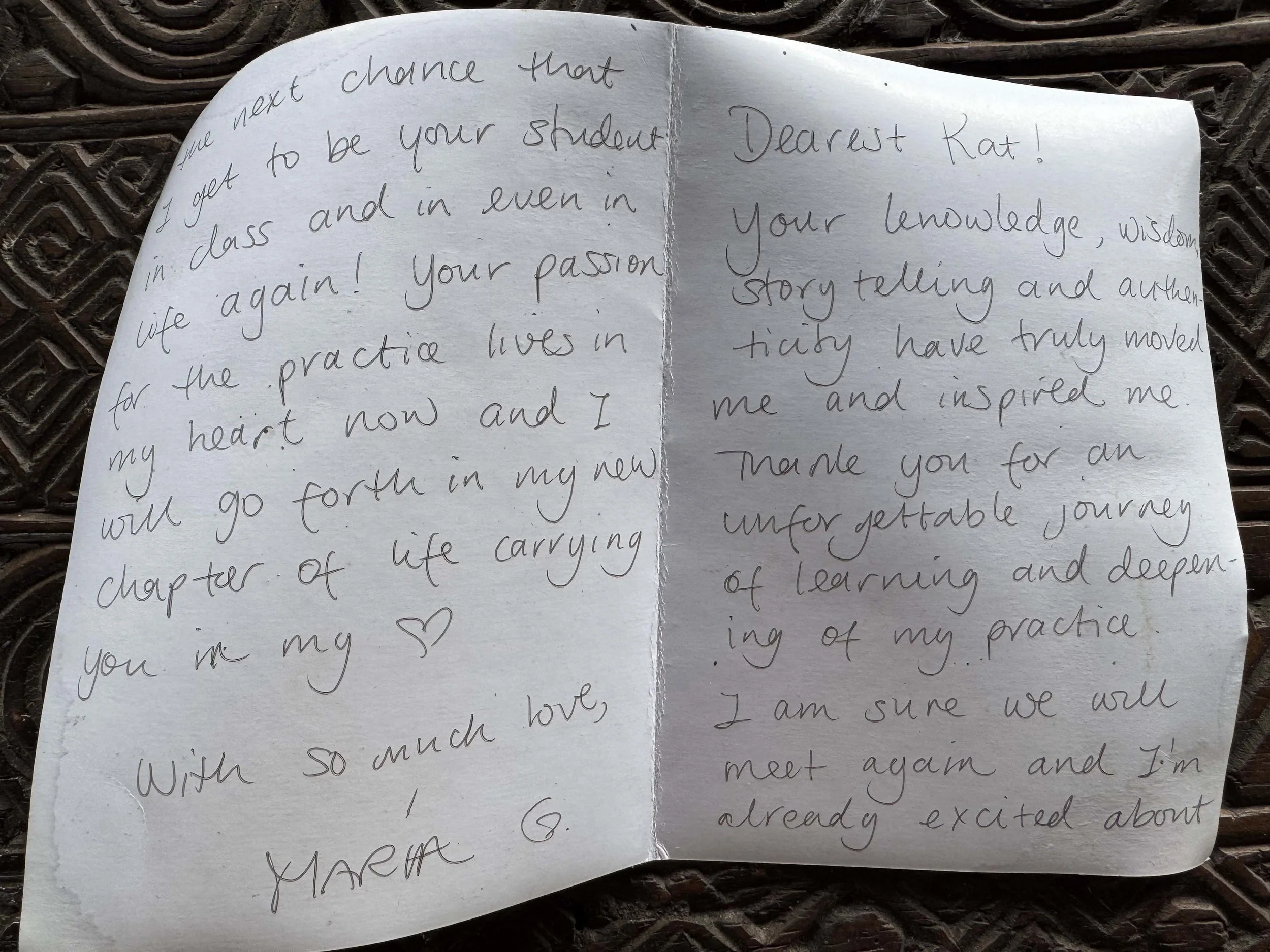A handwritten letter on white paper with cursive writing, placed on a textured, dark wooden surface.
