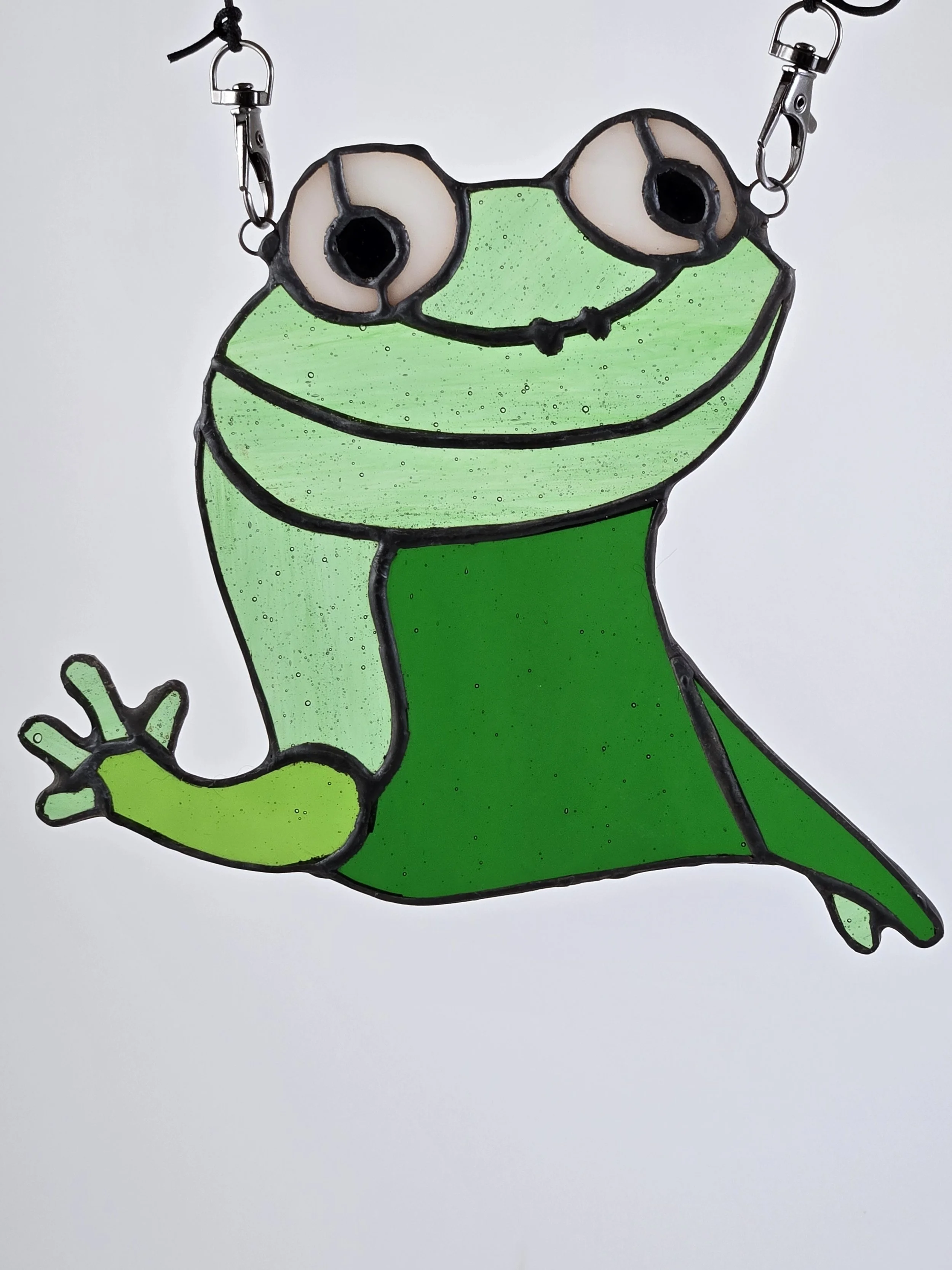 A stained glass sun catcher depicting a lizard with large eyes and a smiling face, hanging by two hooks.