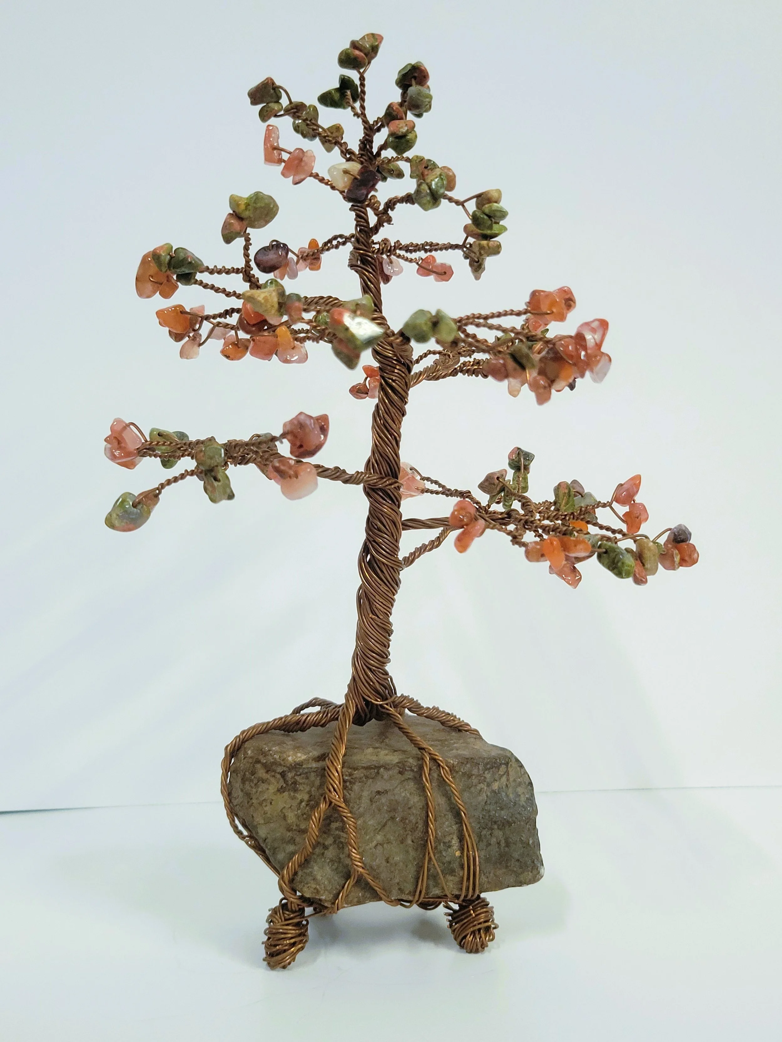 Wire and stone sculpture of a small tree with pink and green stones as leaves, mounted on a rock base.