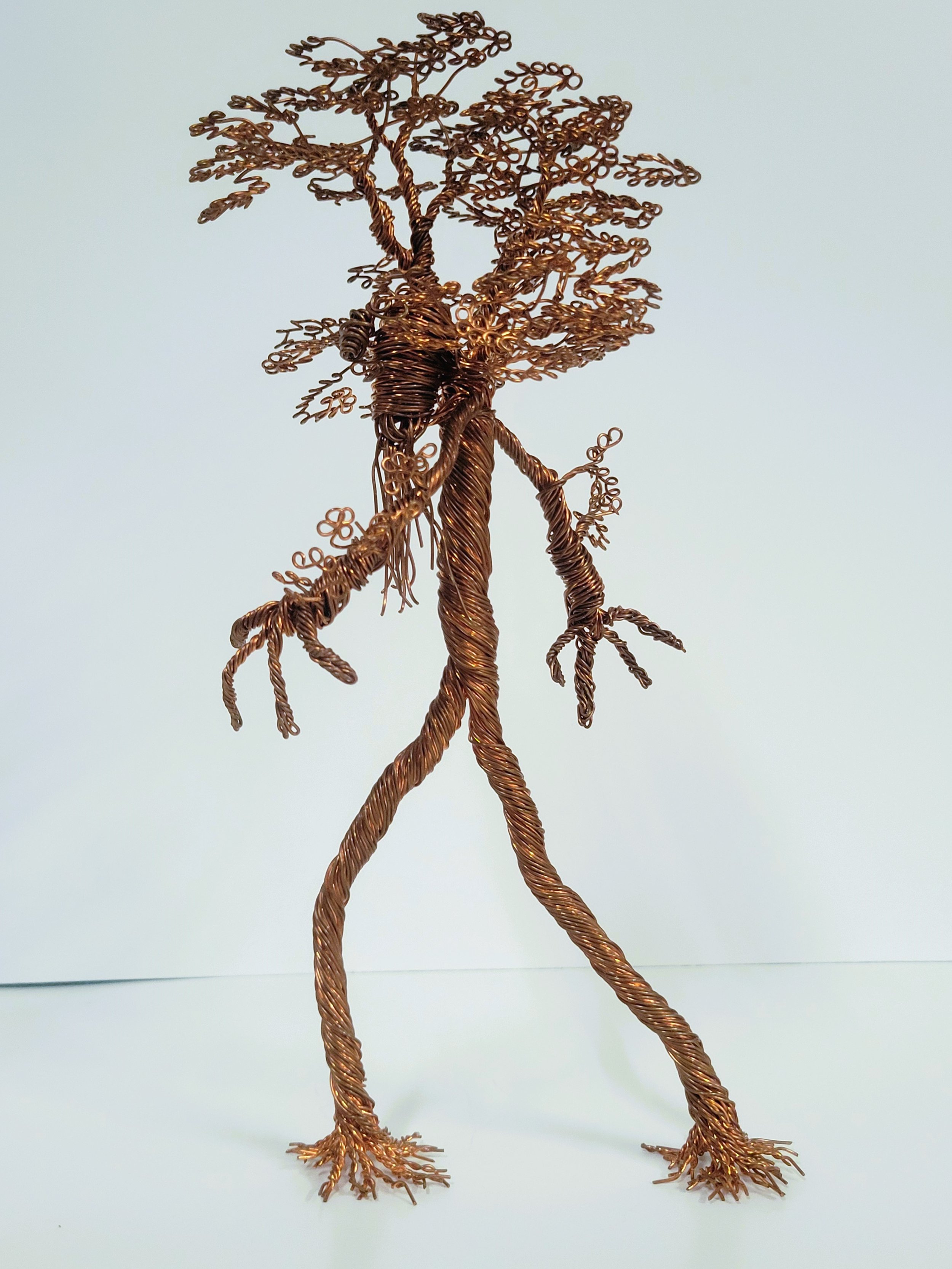 Wire sculpture of a humanoid tree with elongated limbs and abstract features, made from twisted and looped metal wires.