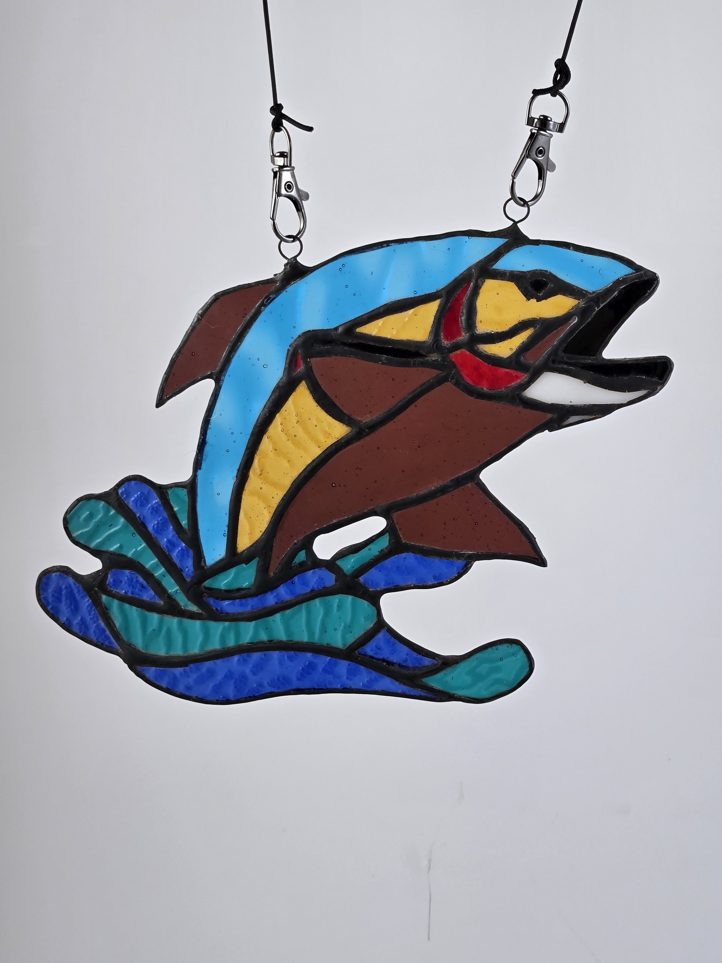 Colorful stained glass suncatcher of a trout jumping out of water on a white background.