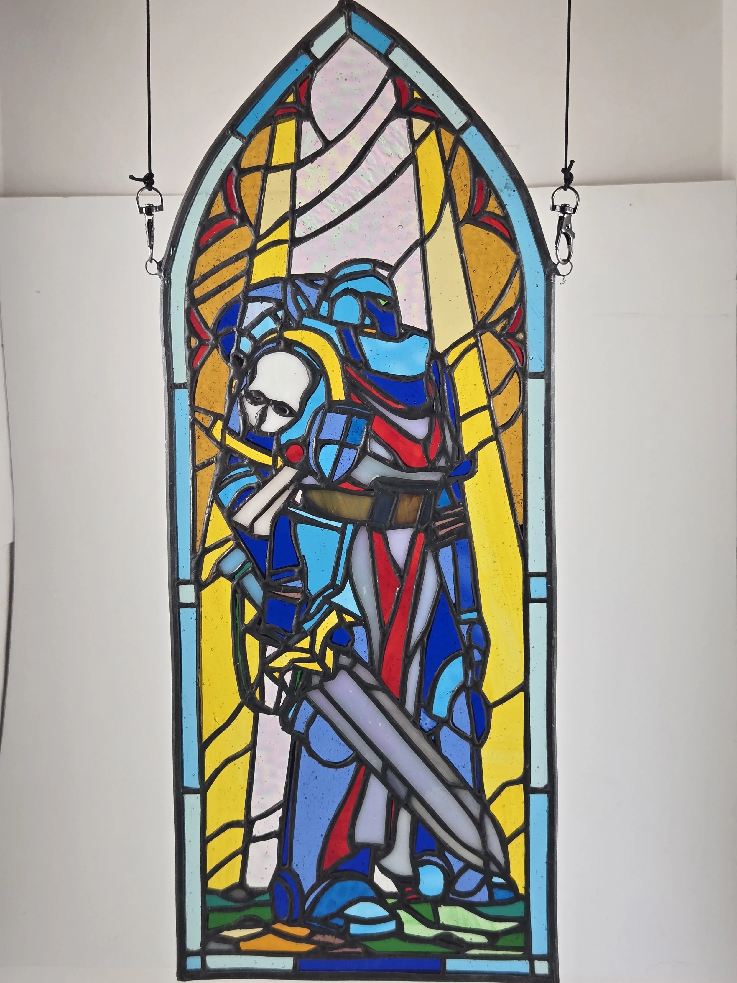 Colorful stained glass peice depicting a knight with a sword and shield, wearing armor and a helmet.