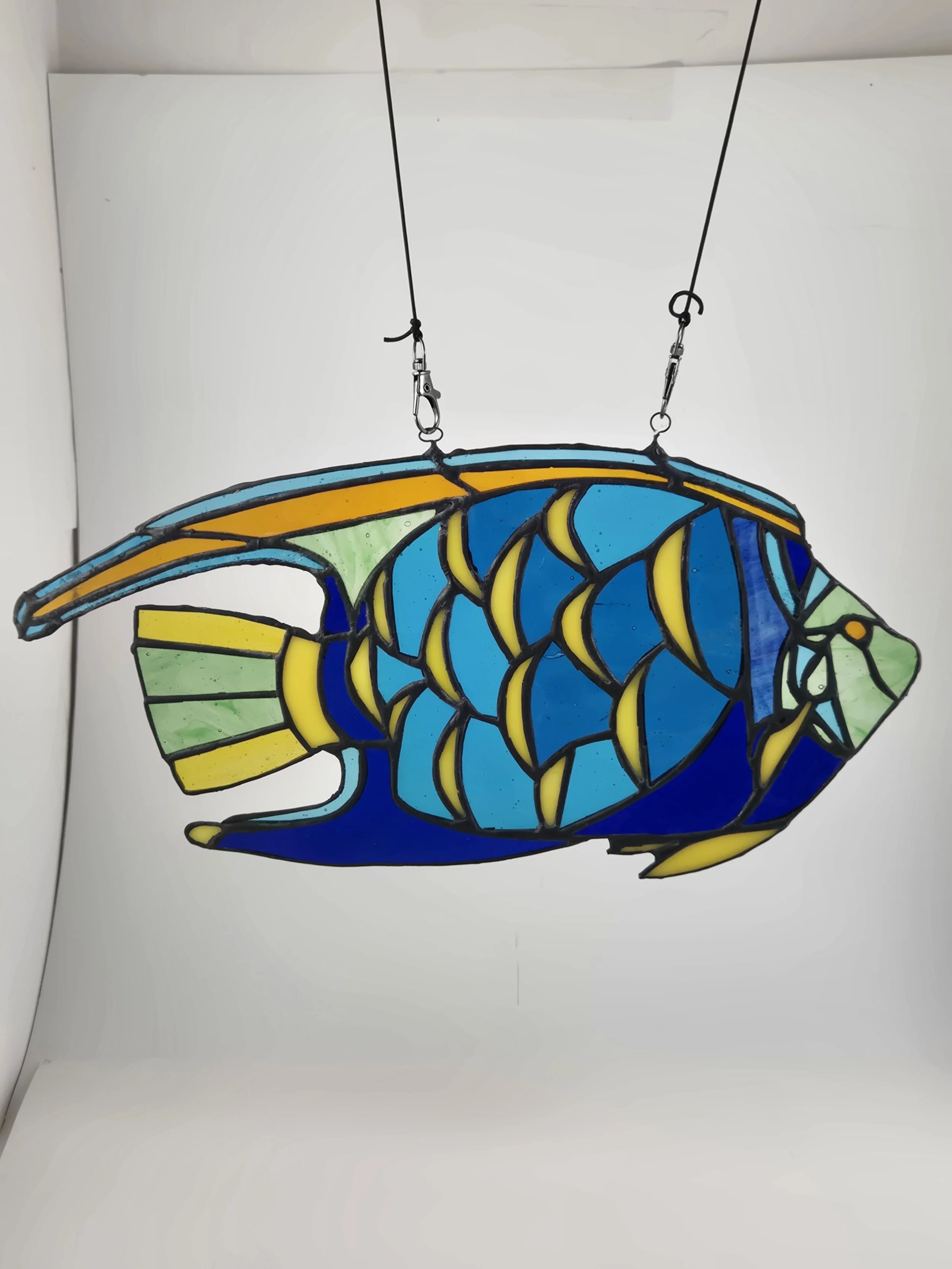 Colorful stained glass piece of a queen angelfish, hanging by two hooks from wires.